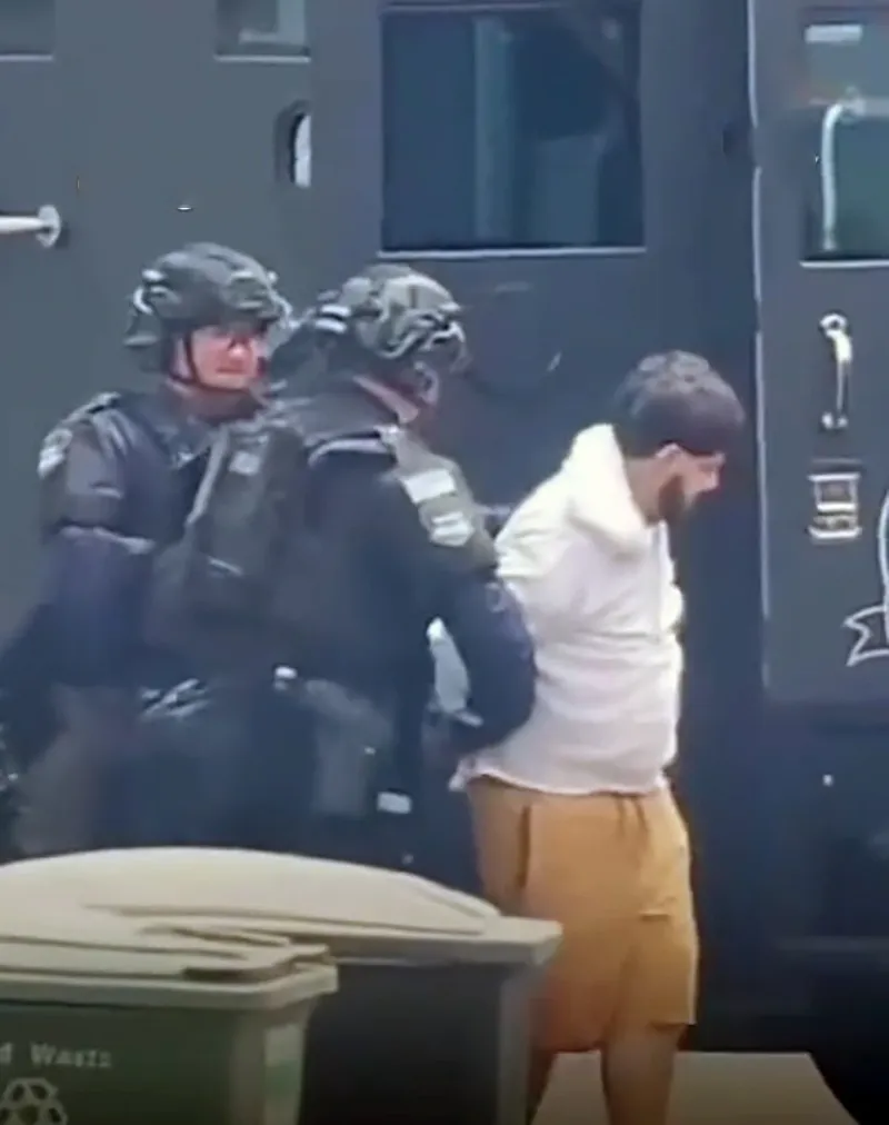 Joaquin Escoto being led away in handcuffs by two officers.