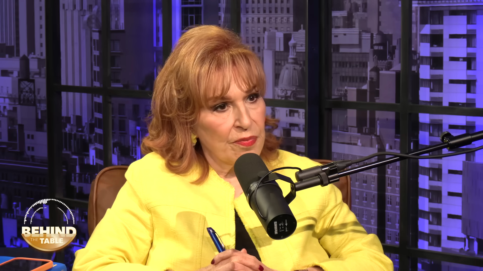 Joy Behar speaking into a microphone during the "Behind the Table" podcast.