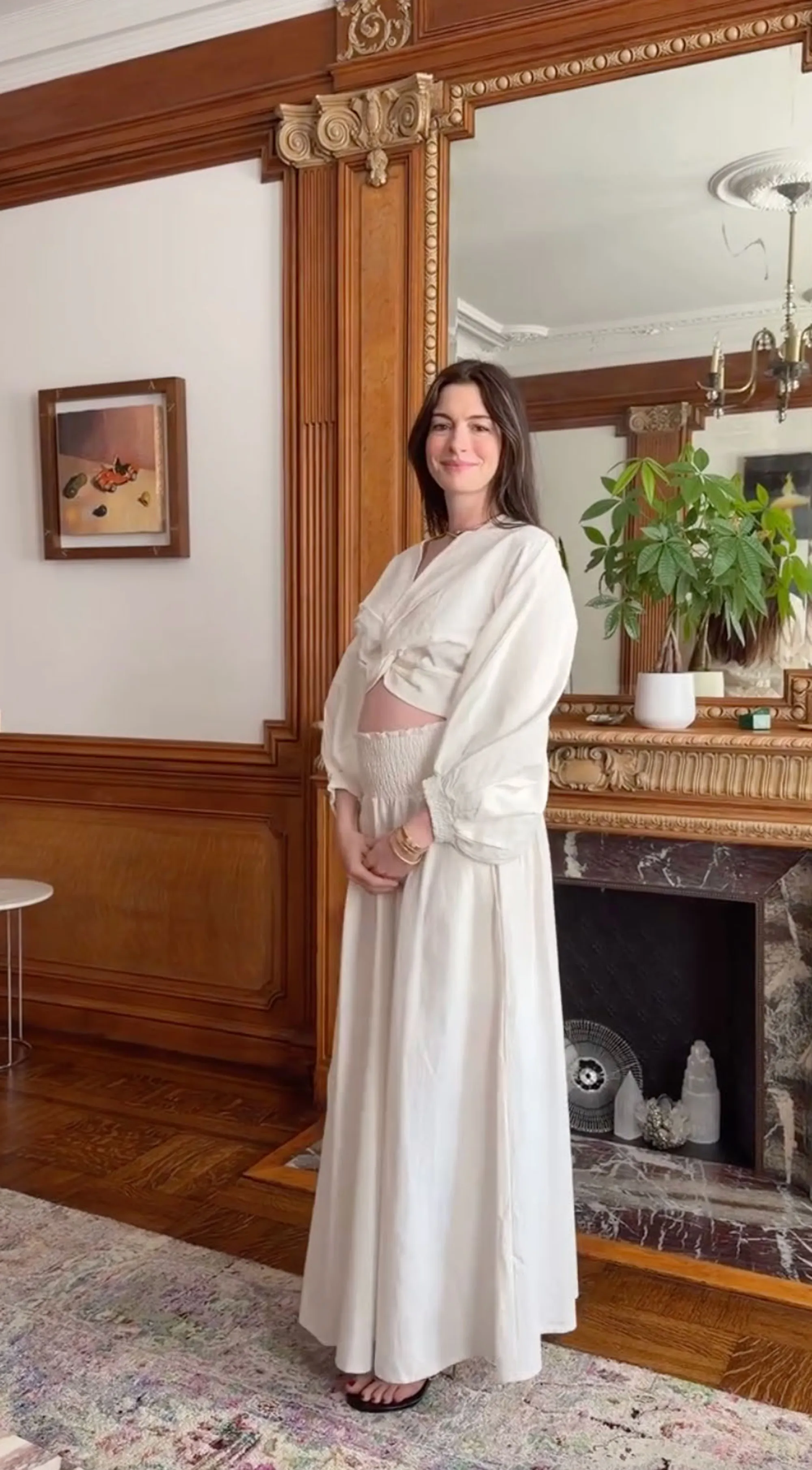 Anne Hathaway showing her pregnant belly in a white outfit.