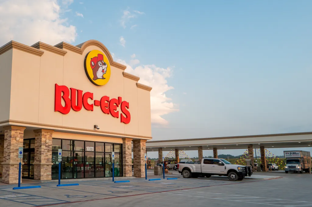 The exterior of a Buc-ee's convenience store with its logo and red lettering, along with a large gas station canopy and vehicles.