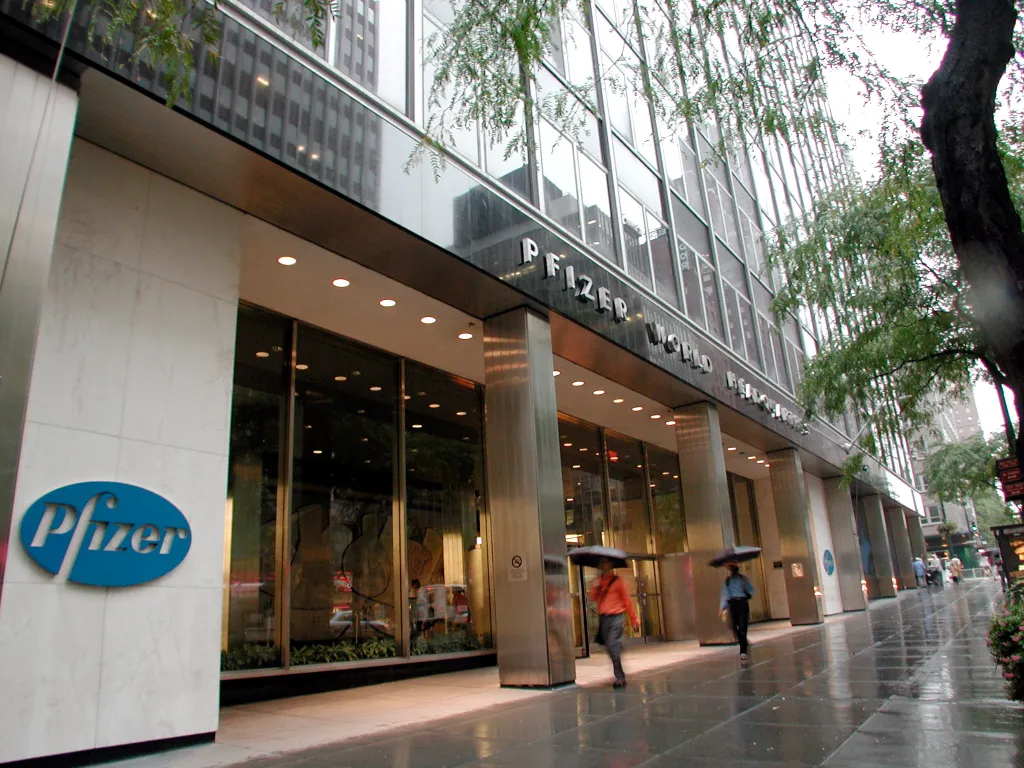 The Pfizer World Headquarters building at 235 E 42nd St, NYC, with the company logo on the left and "PFIZER WORLD HEADQUARTERS" signage above the entrance.