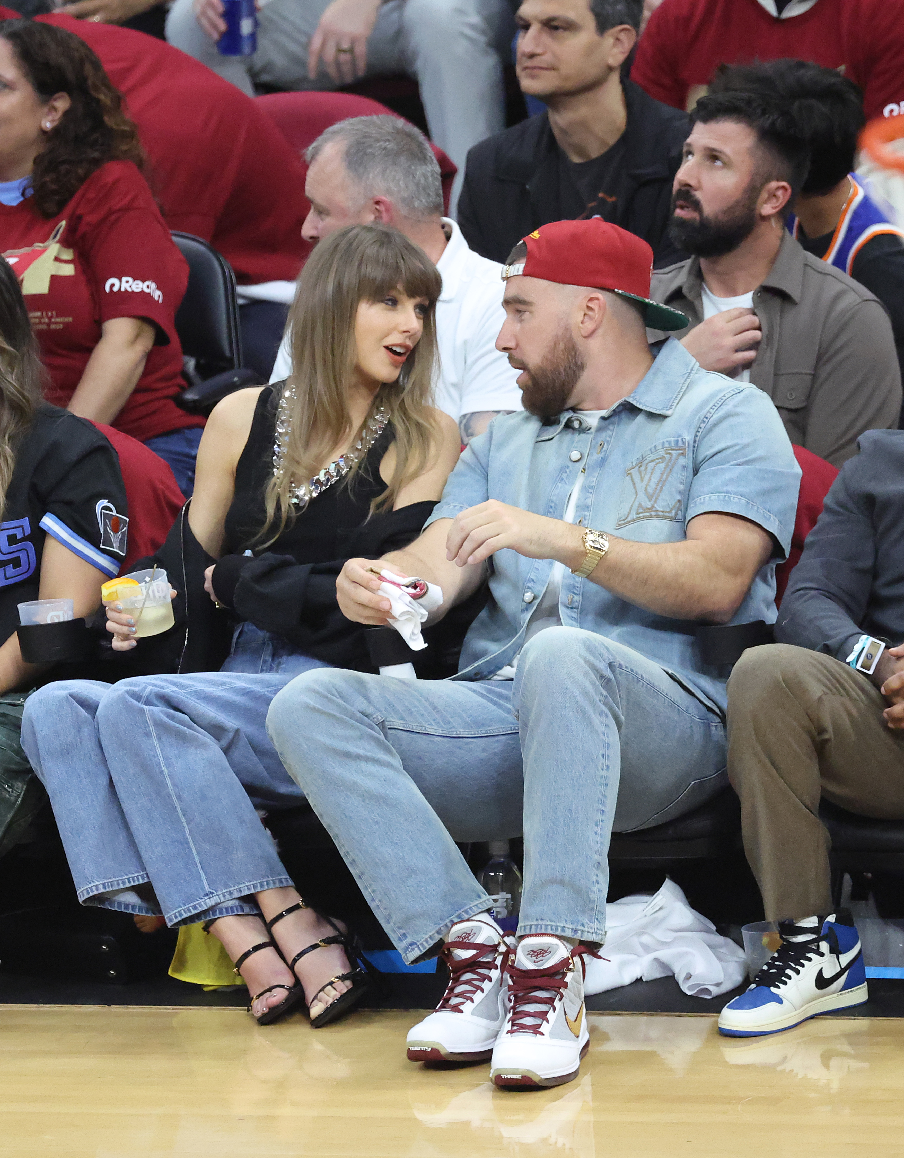 Singer Taylor Swift and Travis Kelce sit courtside at a basketball game.