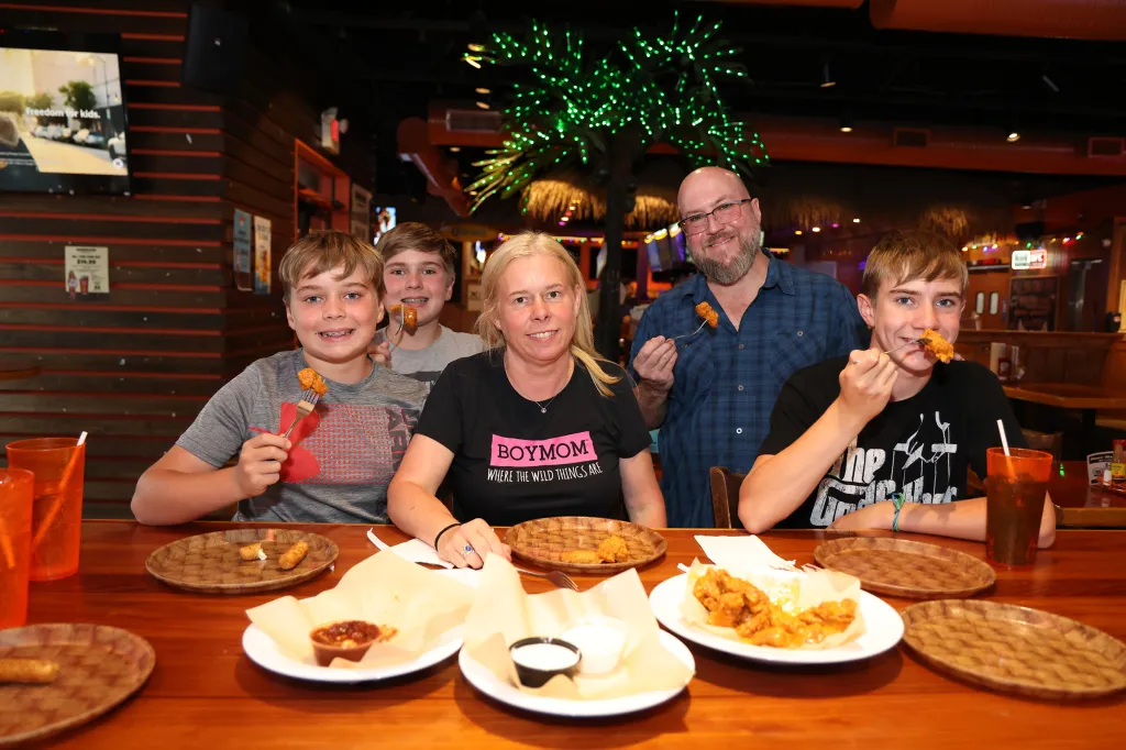 The Llewellyn family sits at a table in the Hooters of Farmingdale, NY restaurant, eating.