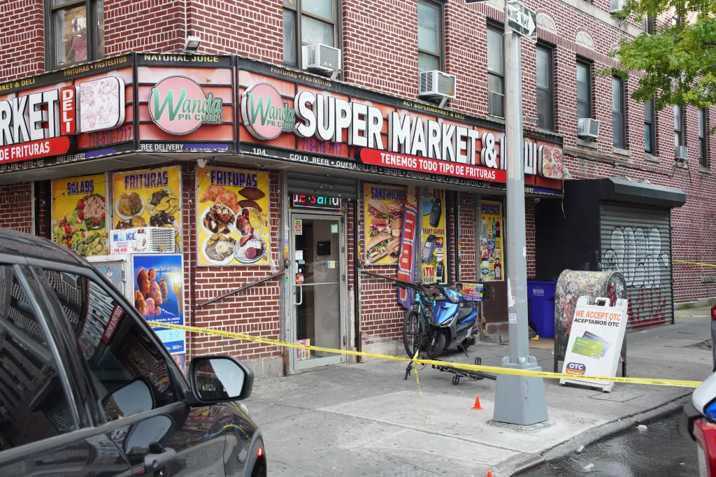 Wanda Super Market & Deli in the Bronx, cordoned off by yellow tape, with a bicycle and scooter near the entrance, following a shooting incident.