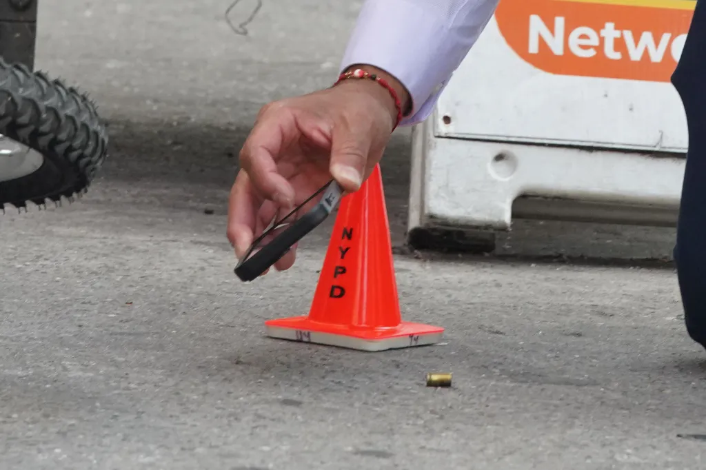 A person photographs a bullet casing next to an NYPD cone.