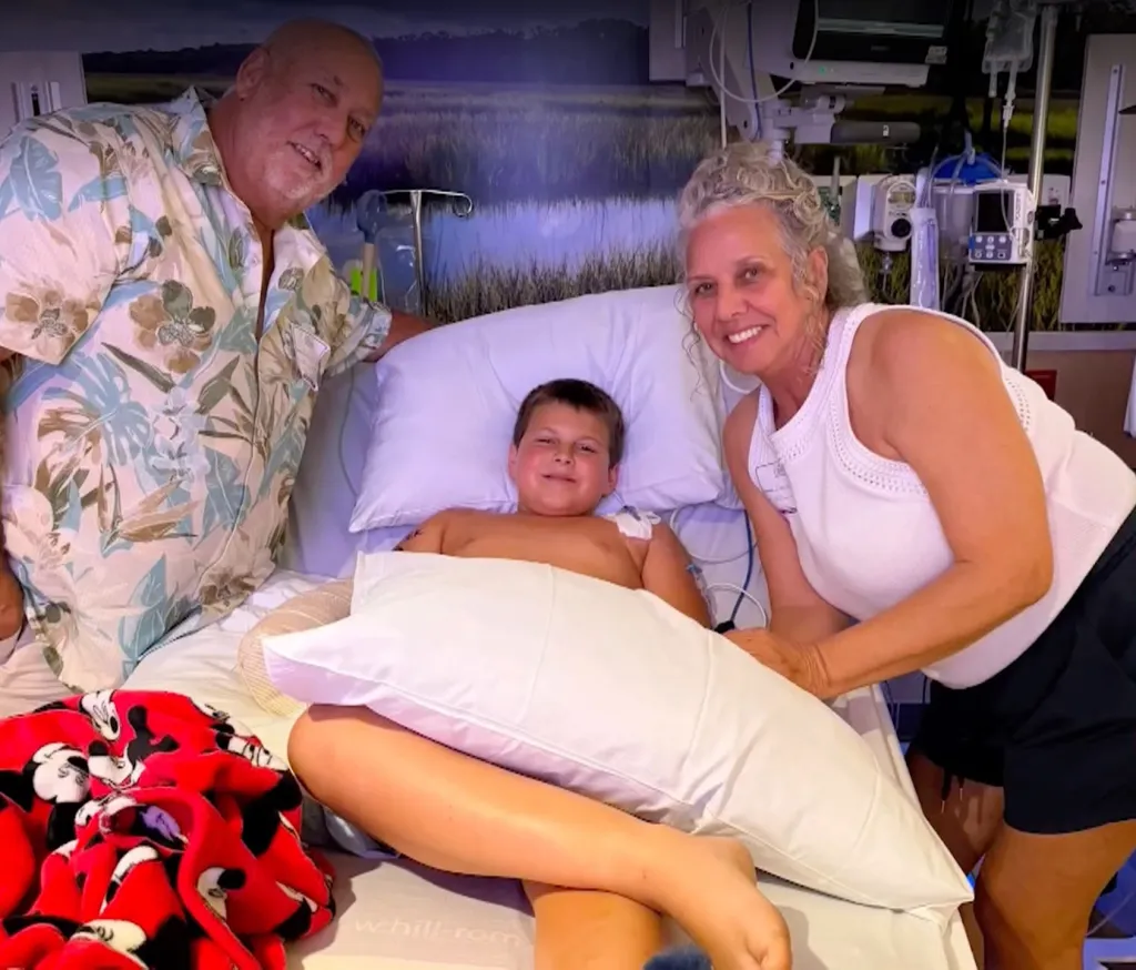 Brodie Terry (center) in a hospital bed with two adults, all smiling at the camera.
