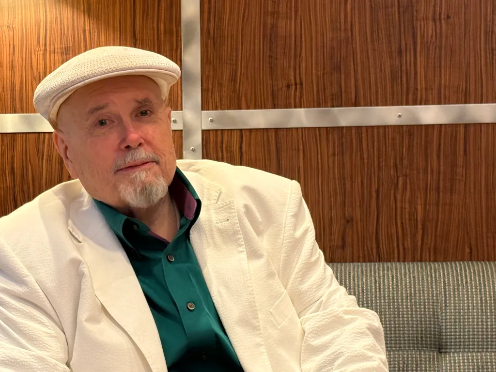 Frank Llewellyn sitting on a couch in a white jacket and green shirt.