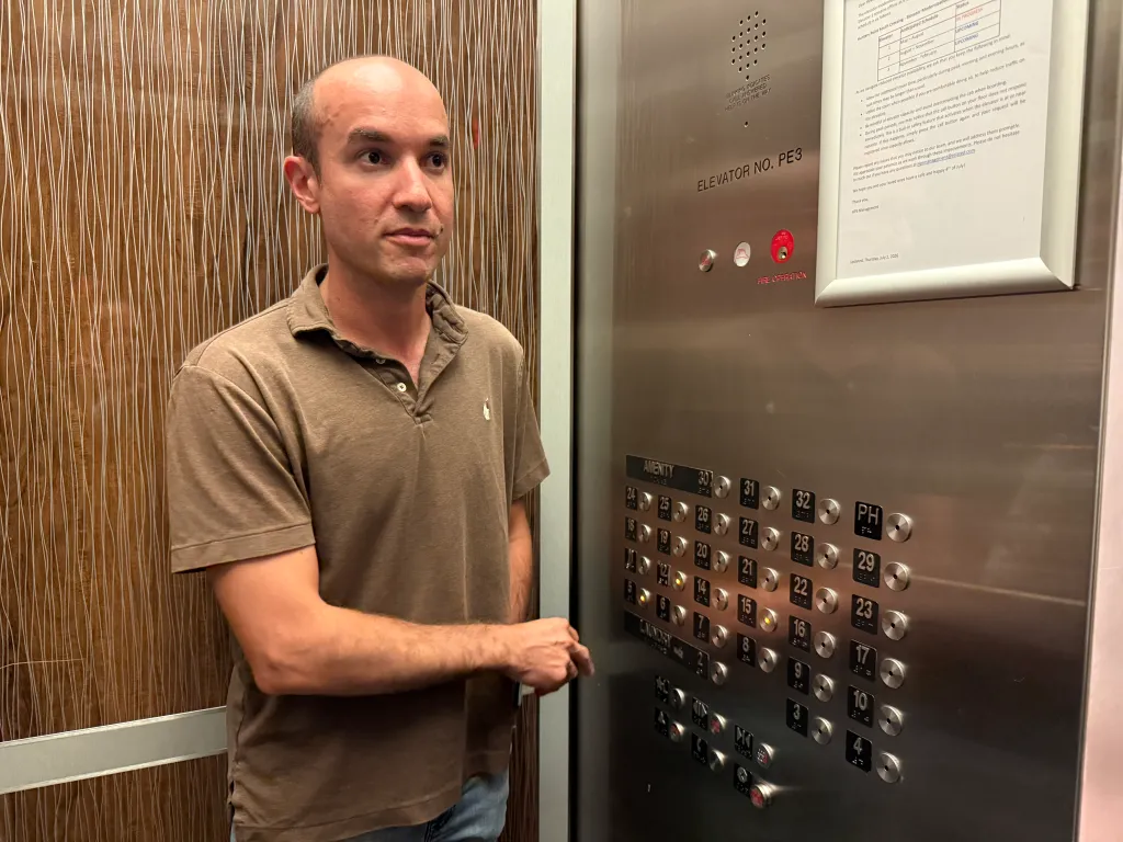 Matt Aaron, head of the tenant association, stands in an elevator with his hand on the control panel.