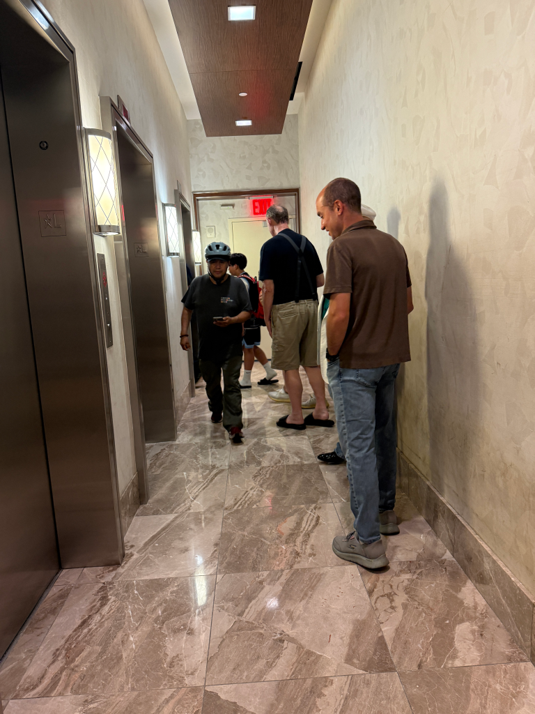 Matt Aaron, head of the tenant association, in a brown shirt, stands with other residents in a hallway with elevators.