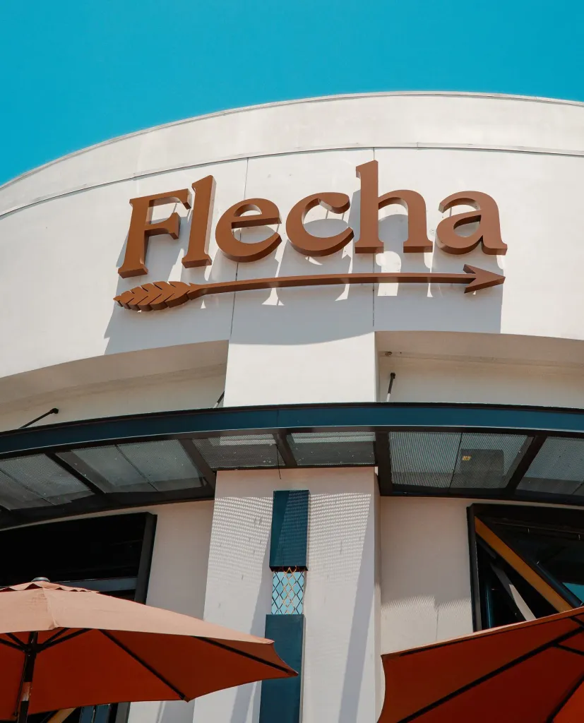 The sign for "Flecha" restaurant, with the letters "Flecha" above a decorative arrow.