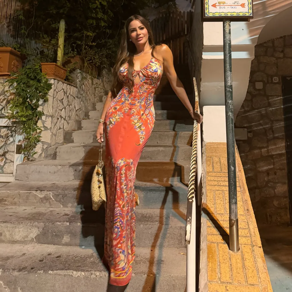 A woman in a floral maxi dress stands on outdoor steps at night.