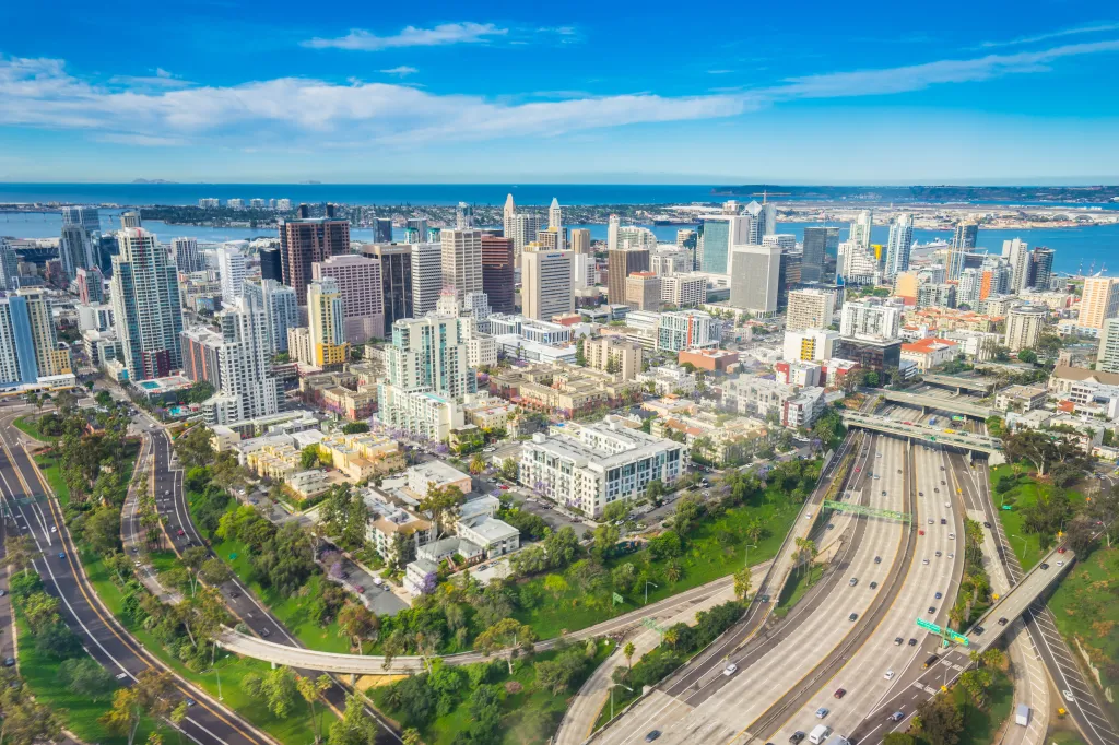 Aerial view of downtown San Diego, California, with highways in the foreground and the bay and ocean in the background.