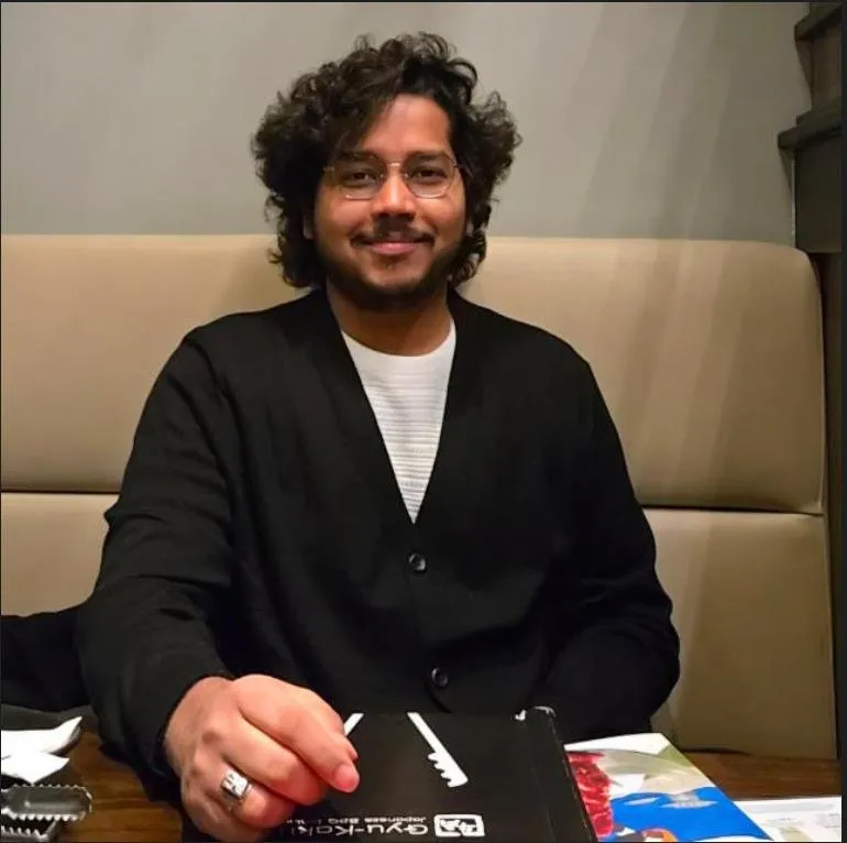 Mani Chandra Teja Gaddam, a man with curly hair and glasses, smiling while sitting at a table.