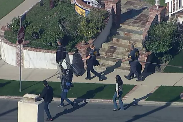 Law enforcement officials leaving a house while carrying evidence.