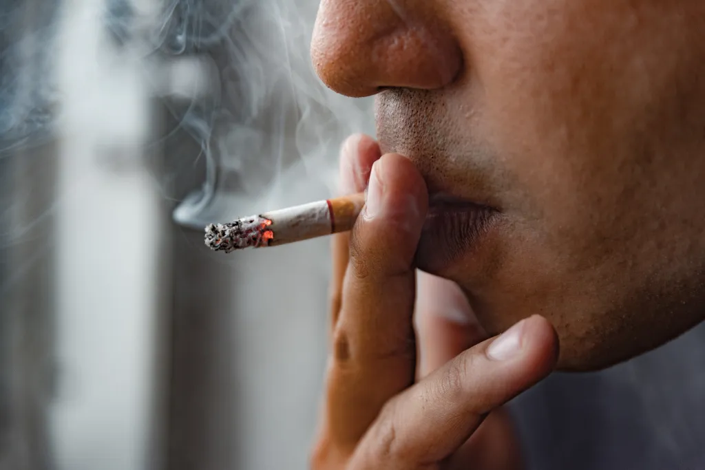 Close up male hand holding a smoking cigarette to his mouth.