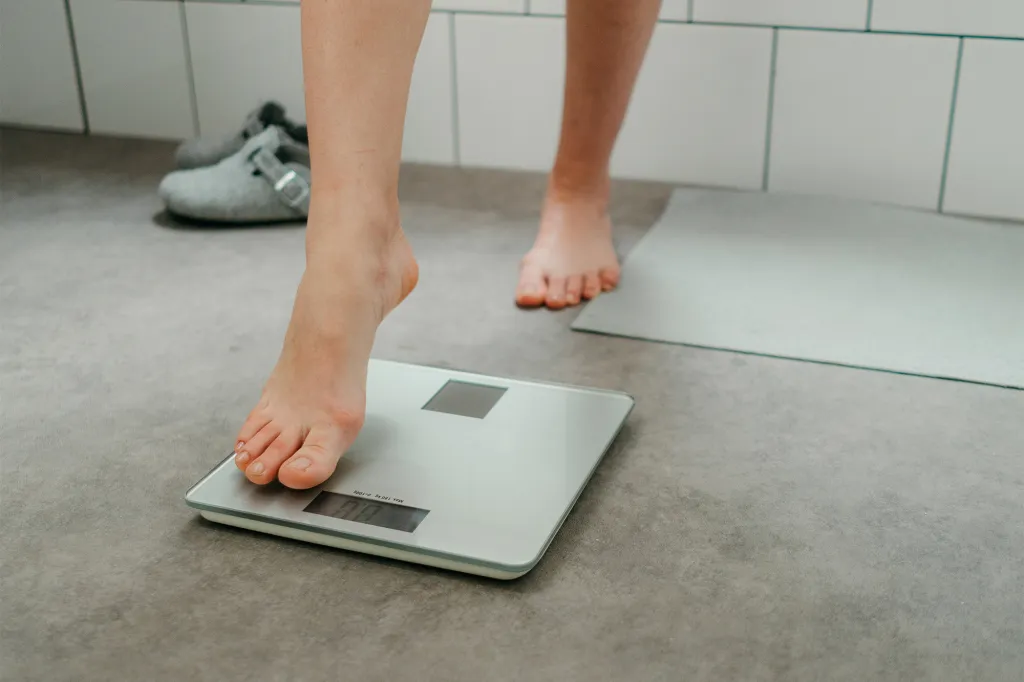 A person's bare feet stepping onto a digital bathroom scale.