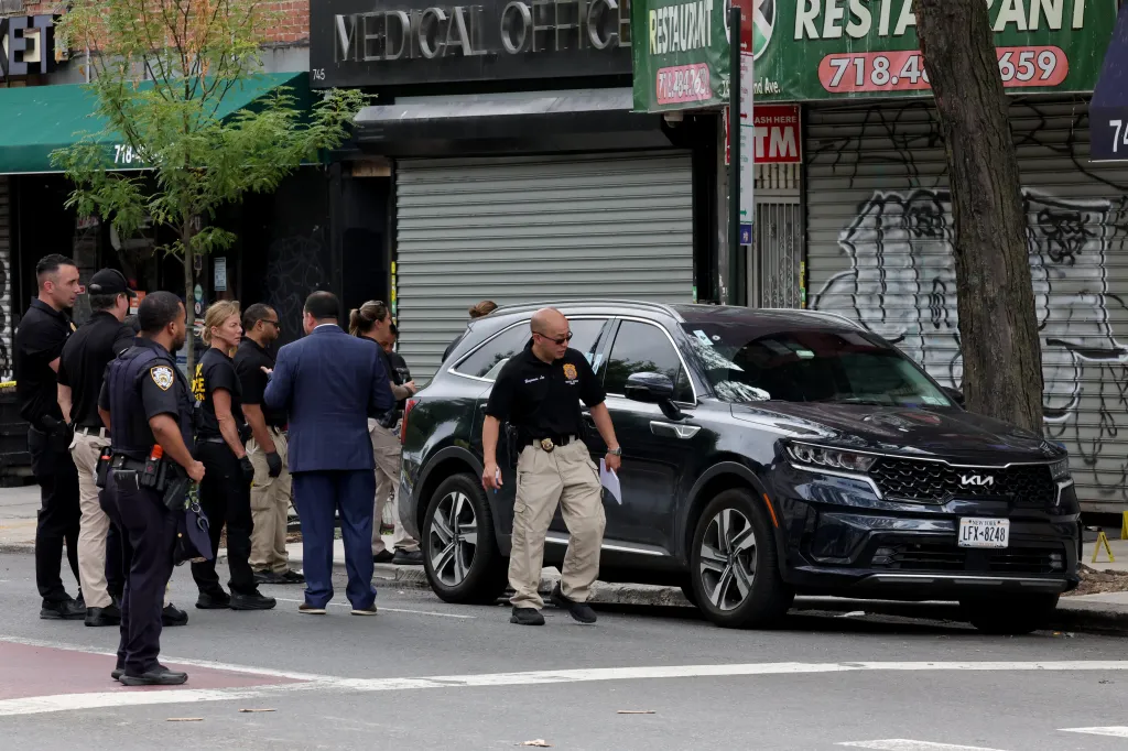 NYPD Crime Scene Unit detectives examine an unmarked police vehicle with a bullet hole in the windshield.