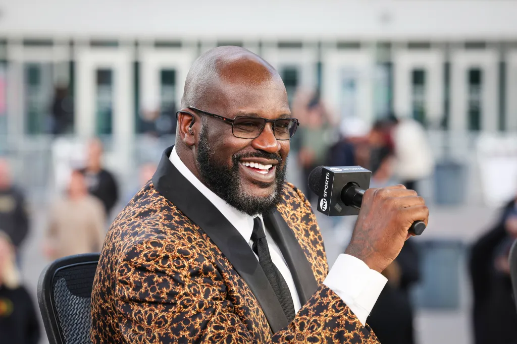 Shaquille O'Neal holding a TNT Sports microphone while smiling at the NBA Cup Semifinals.