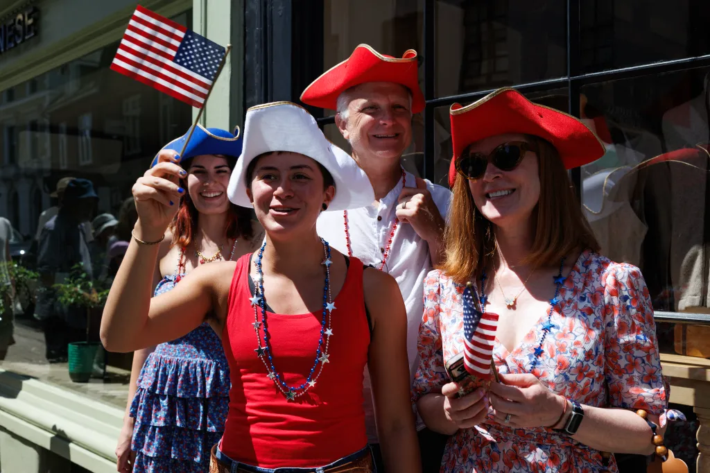 Tourists wearing tricorne hats and star-spangled necklaces wave American flags during a procession outside Bull House in Lewes, England.