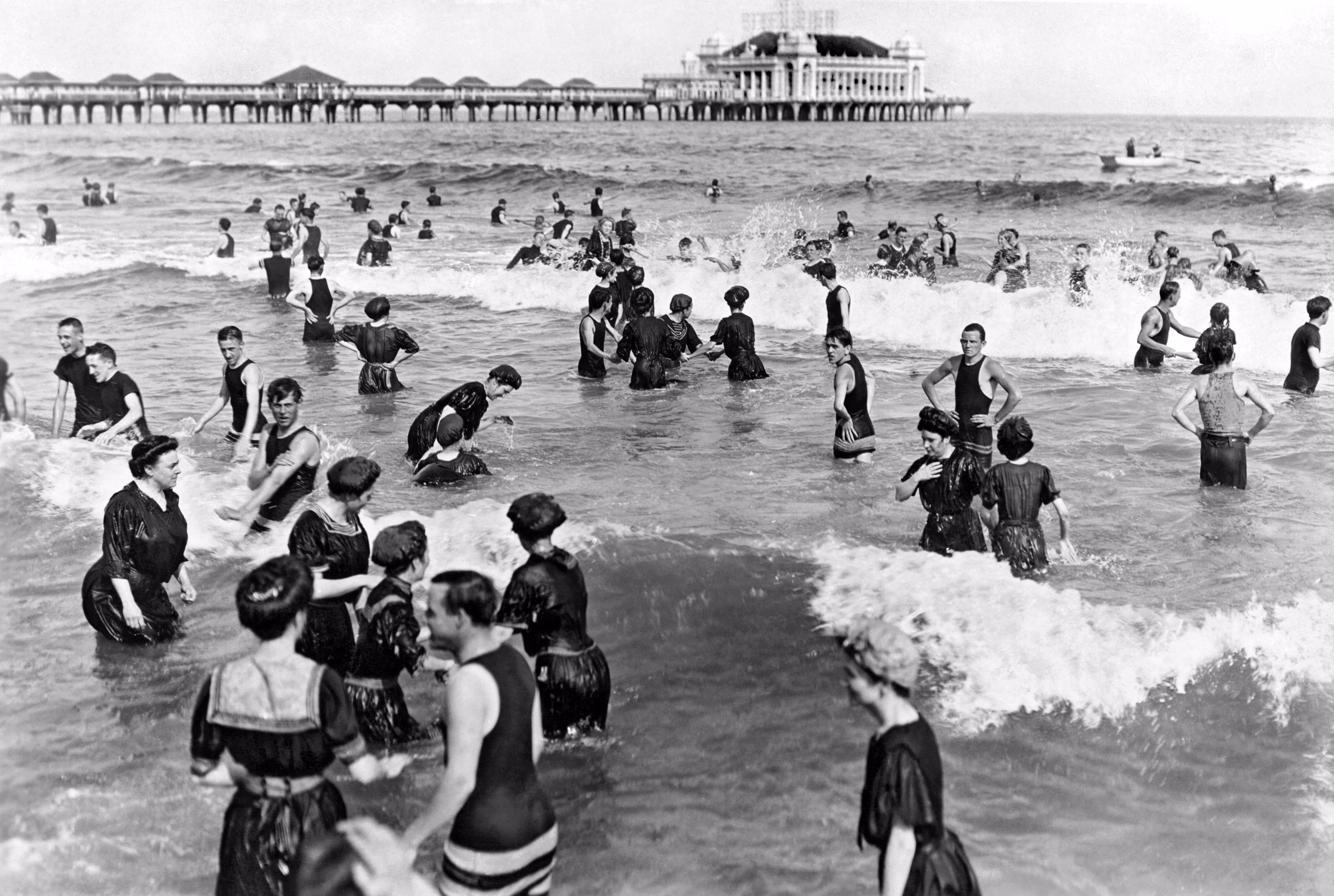 Dozens of people in long bathing costumes play in the surf in 1911.