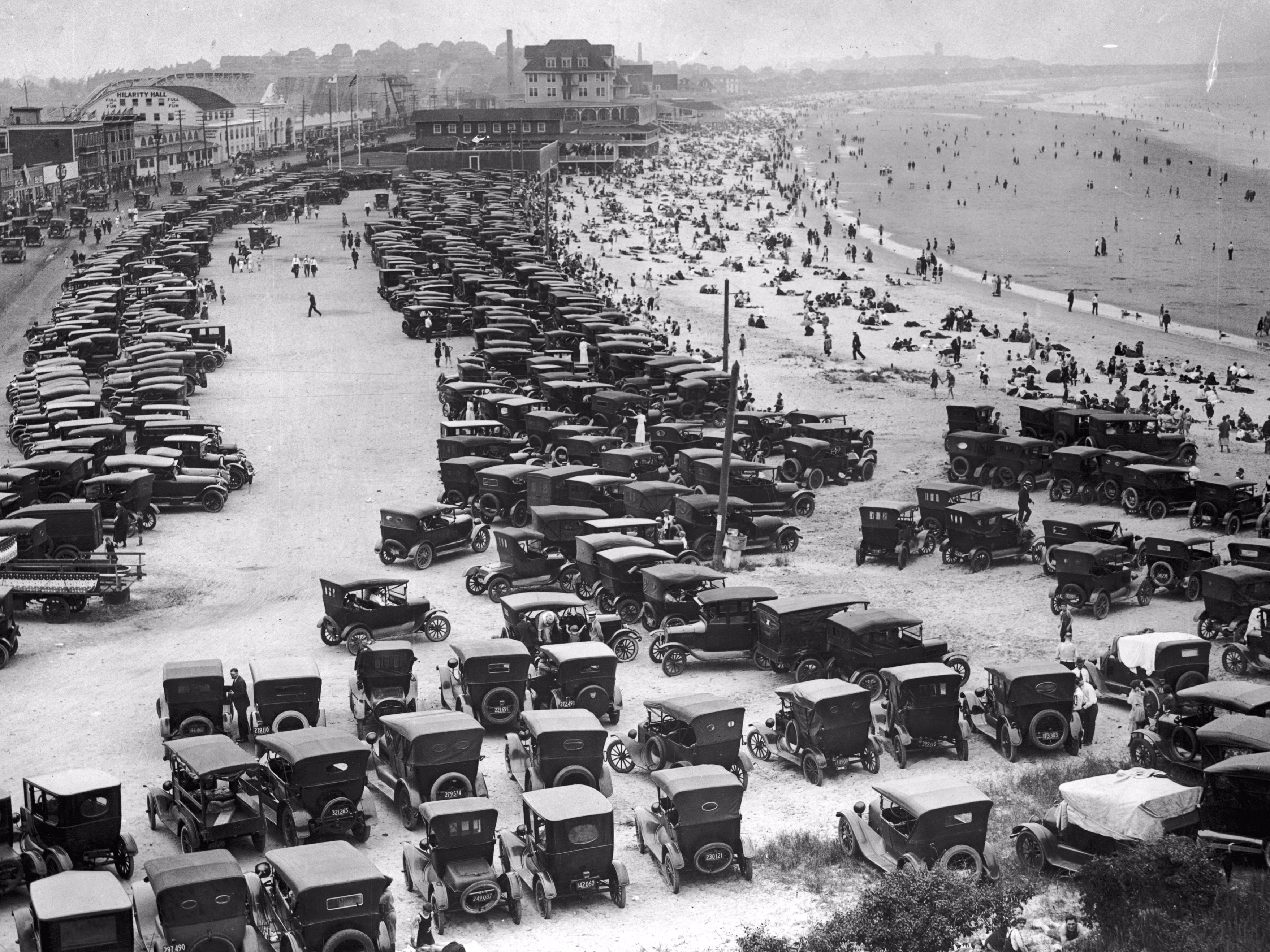 Hundreds of 1920s-era automobiles, parked near a busy beach