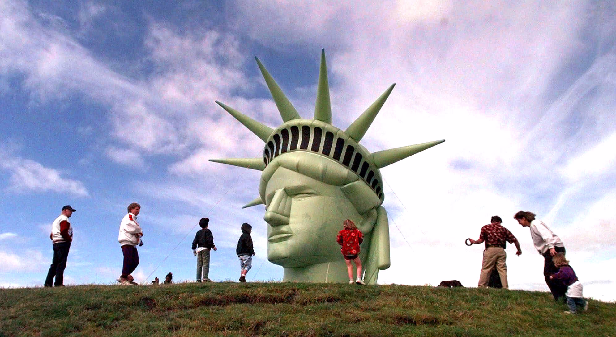 Visitors walk past a balloon replica of the head of the Statue of Liberty.