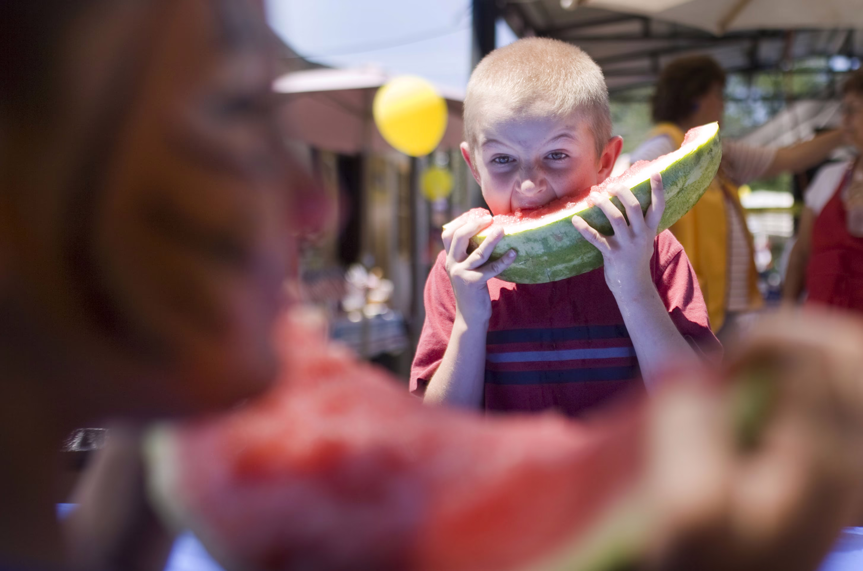 A boy energetically eats a large slice of watermelon during a contest.