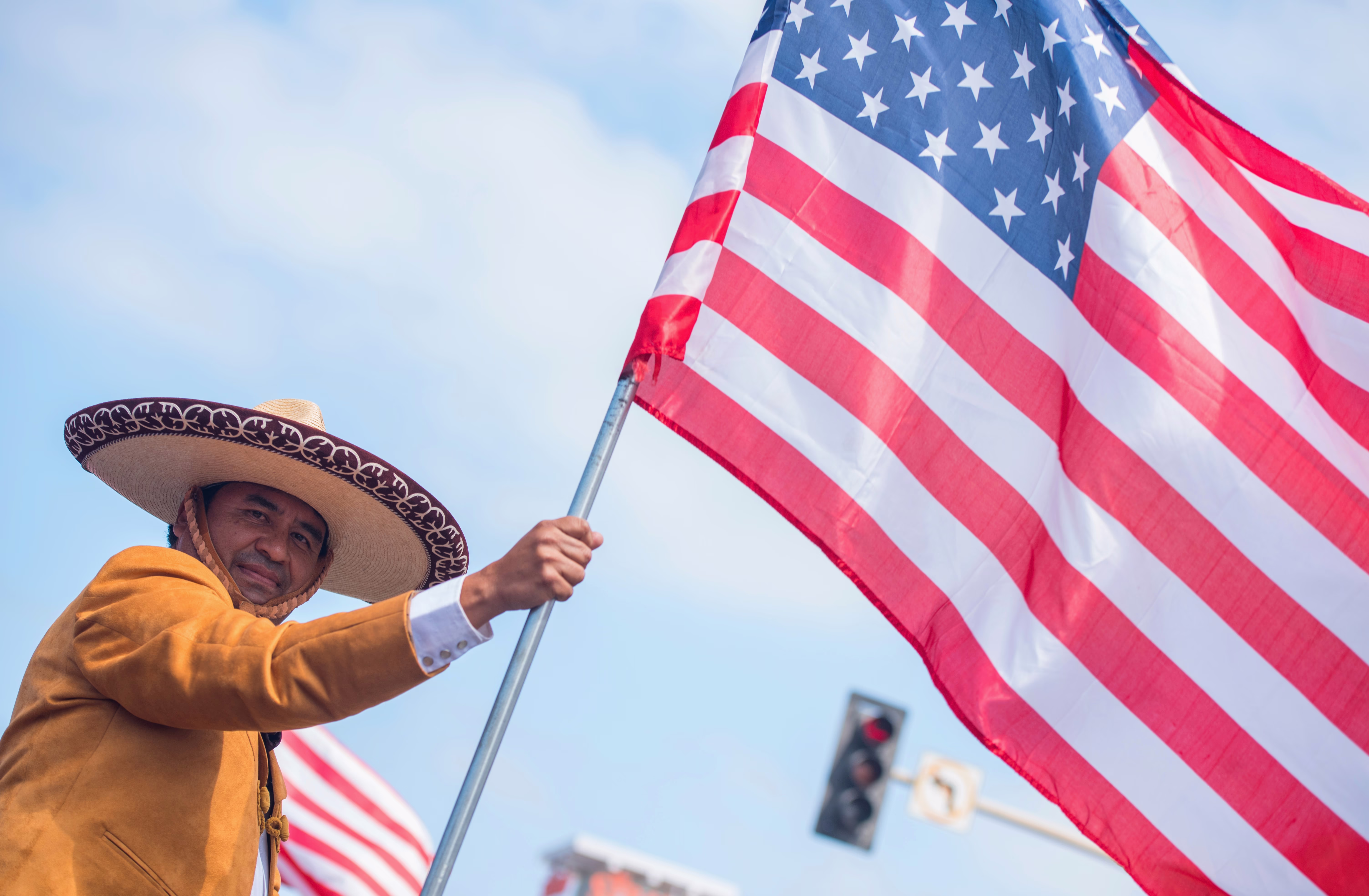 A person wears a sombrero, waving an American flag during a parade.