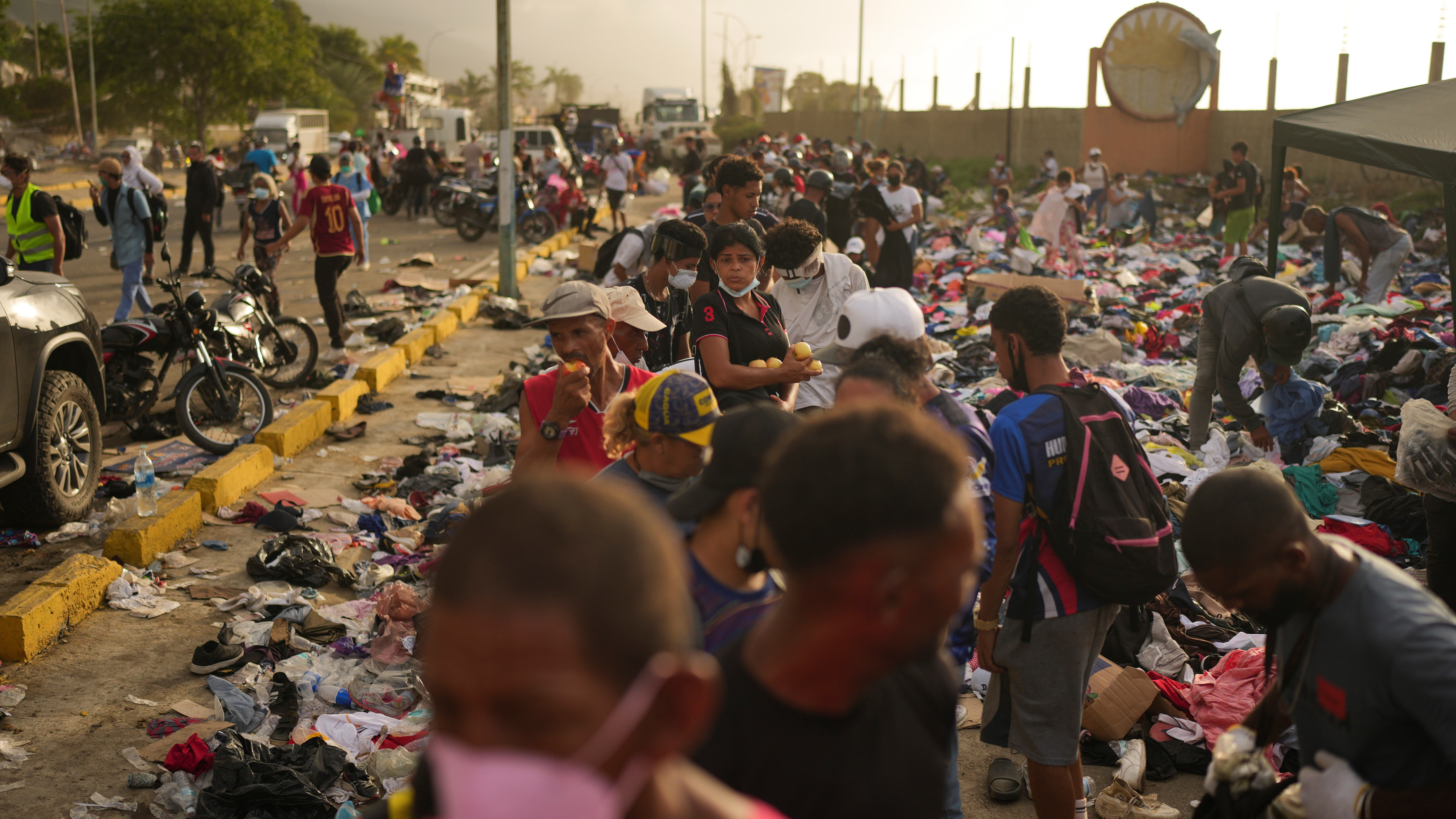 A color photograph shows people lining up for food on the side of a road carpeted with trash in La Guaira, Venezuela.