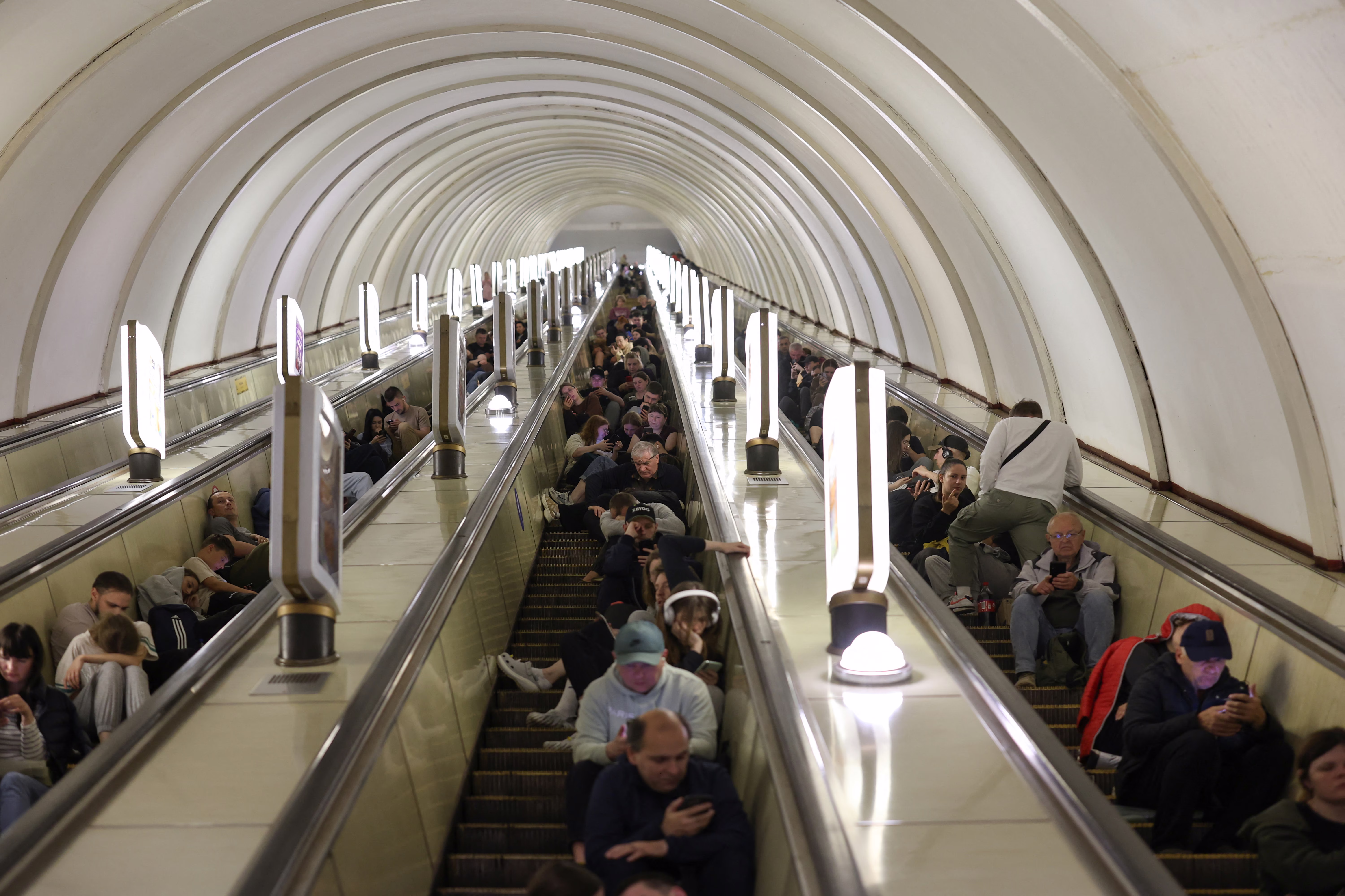 People take shelter, sitting on escalators in a metro station during a missile strike.