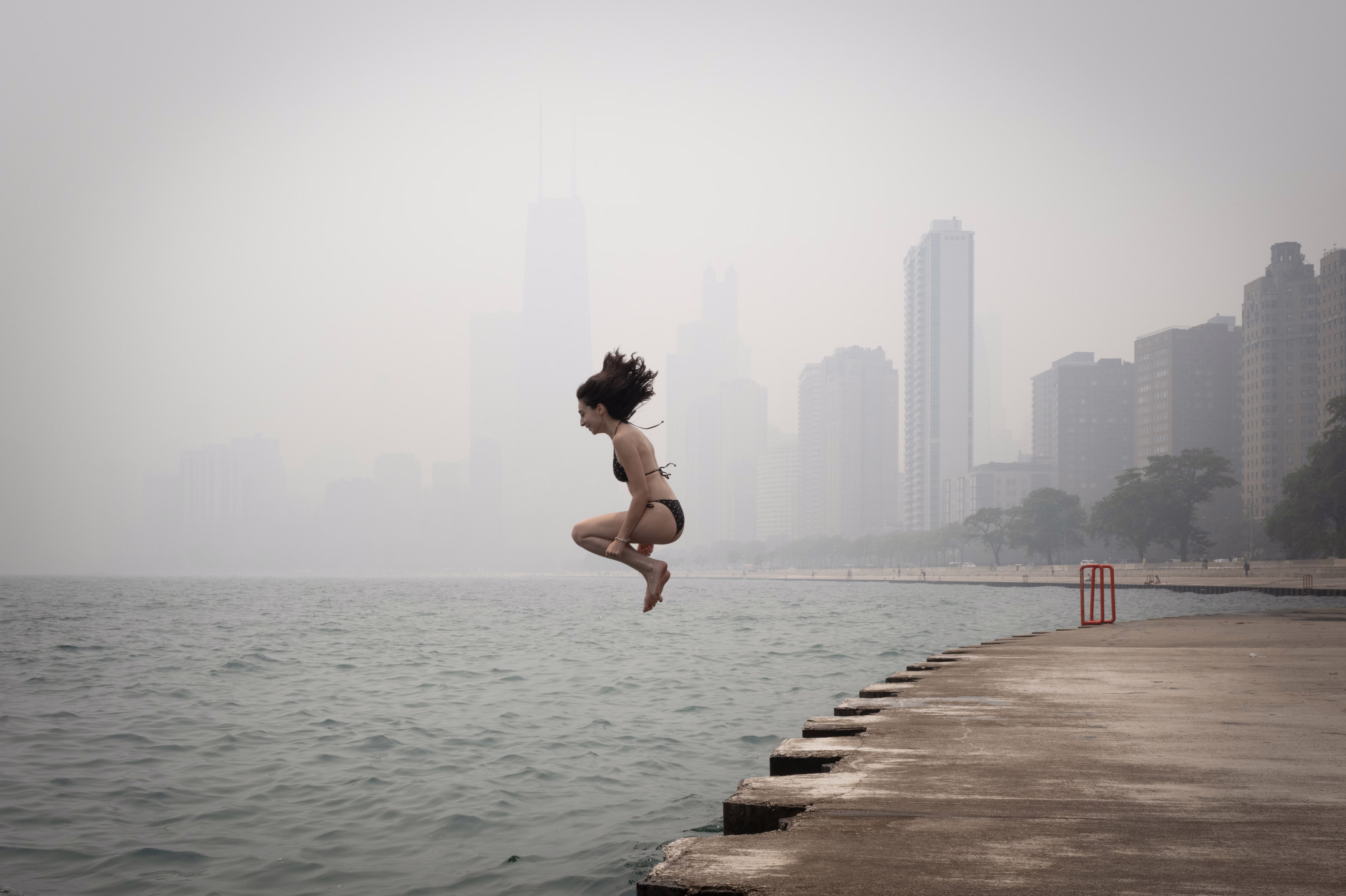 A person jumps into Lake Michigan, with Chicago buildings in the background obscured by a smoke-filled sky.