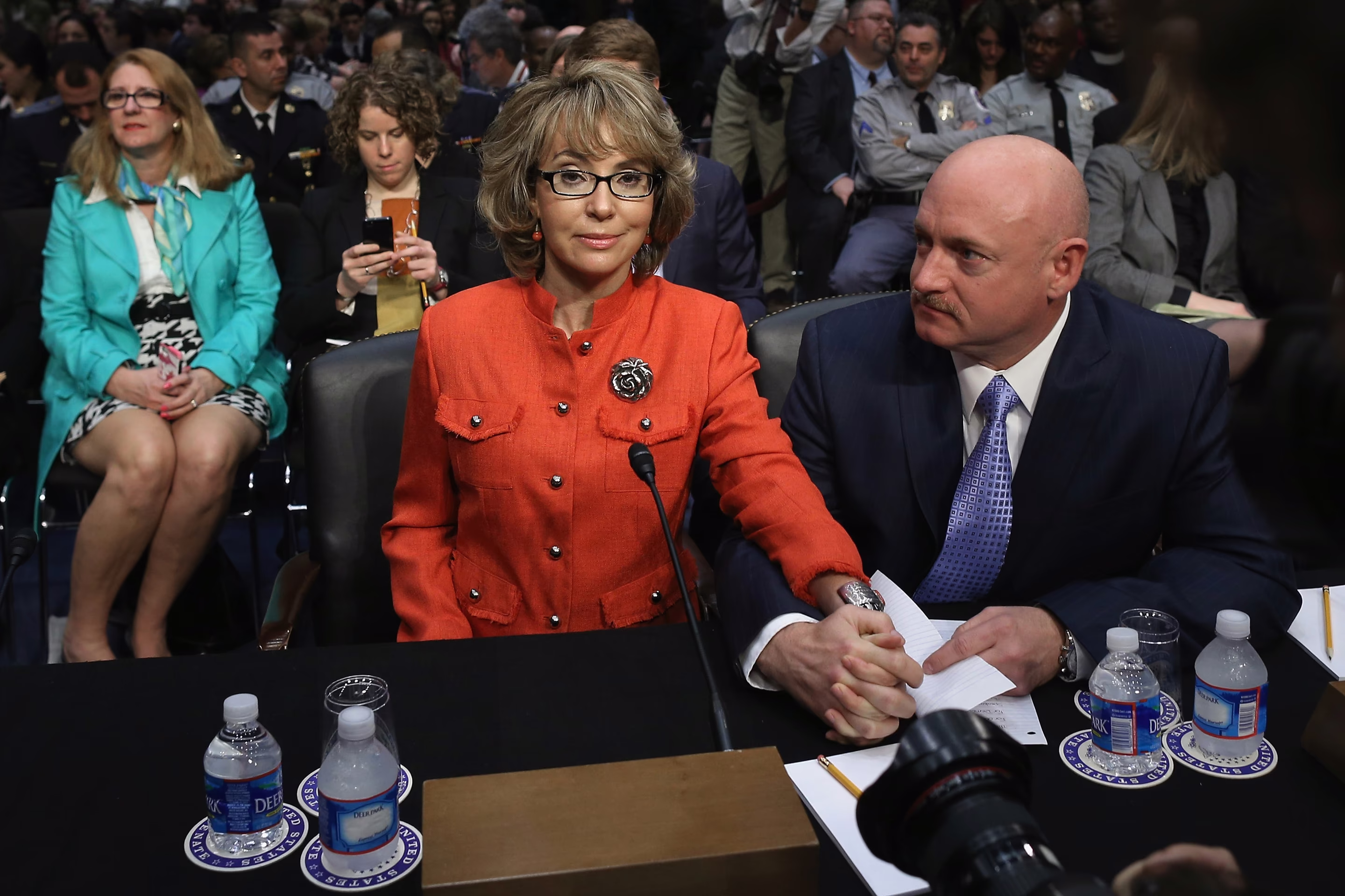 a woman and man sit at a table with people behind them
