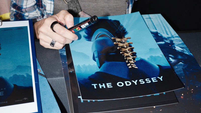 A photo of a pile of posters for 'The Odyssey' showing a Greek soldier in armor from behind.