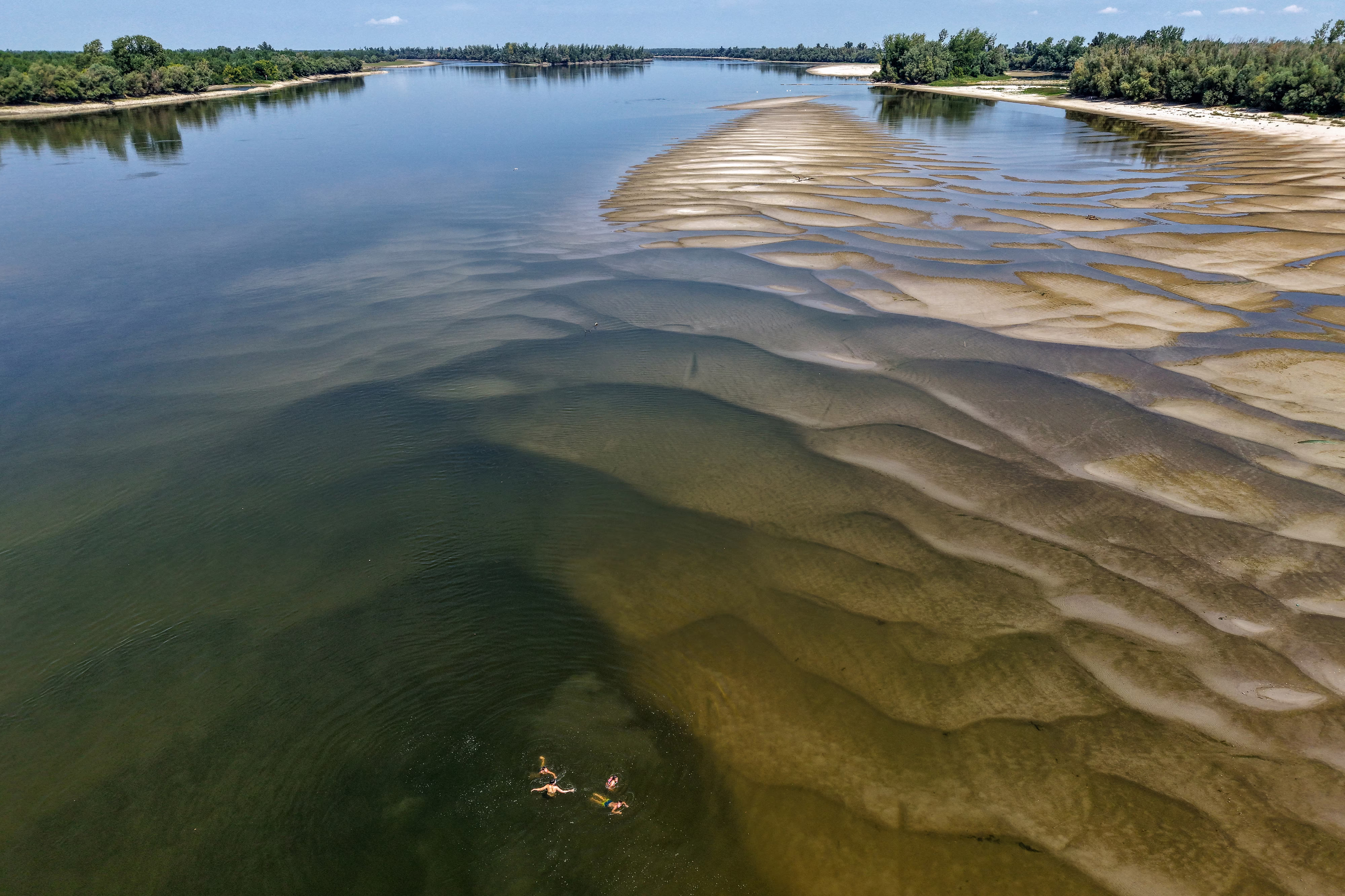 An aerial view of low water levels in the Danube River, with several people swimming at the bottom of the photo.
