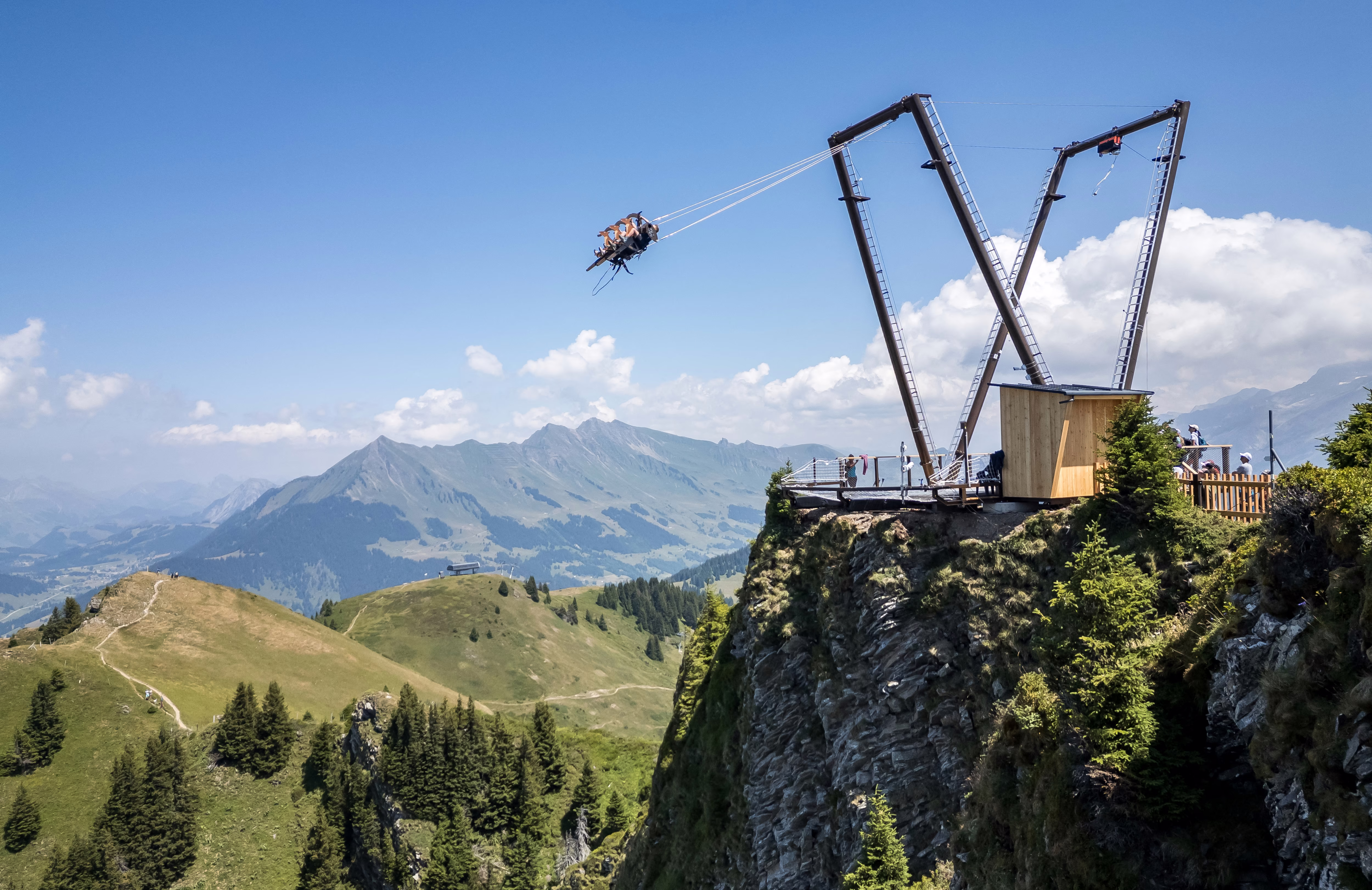 People ride on a giant swing set on the edge of a cliff high in the mountains.