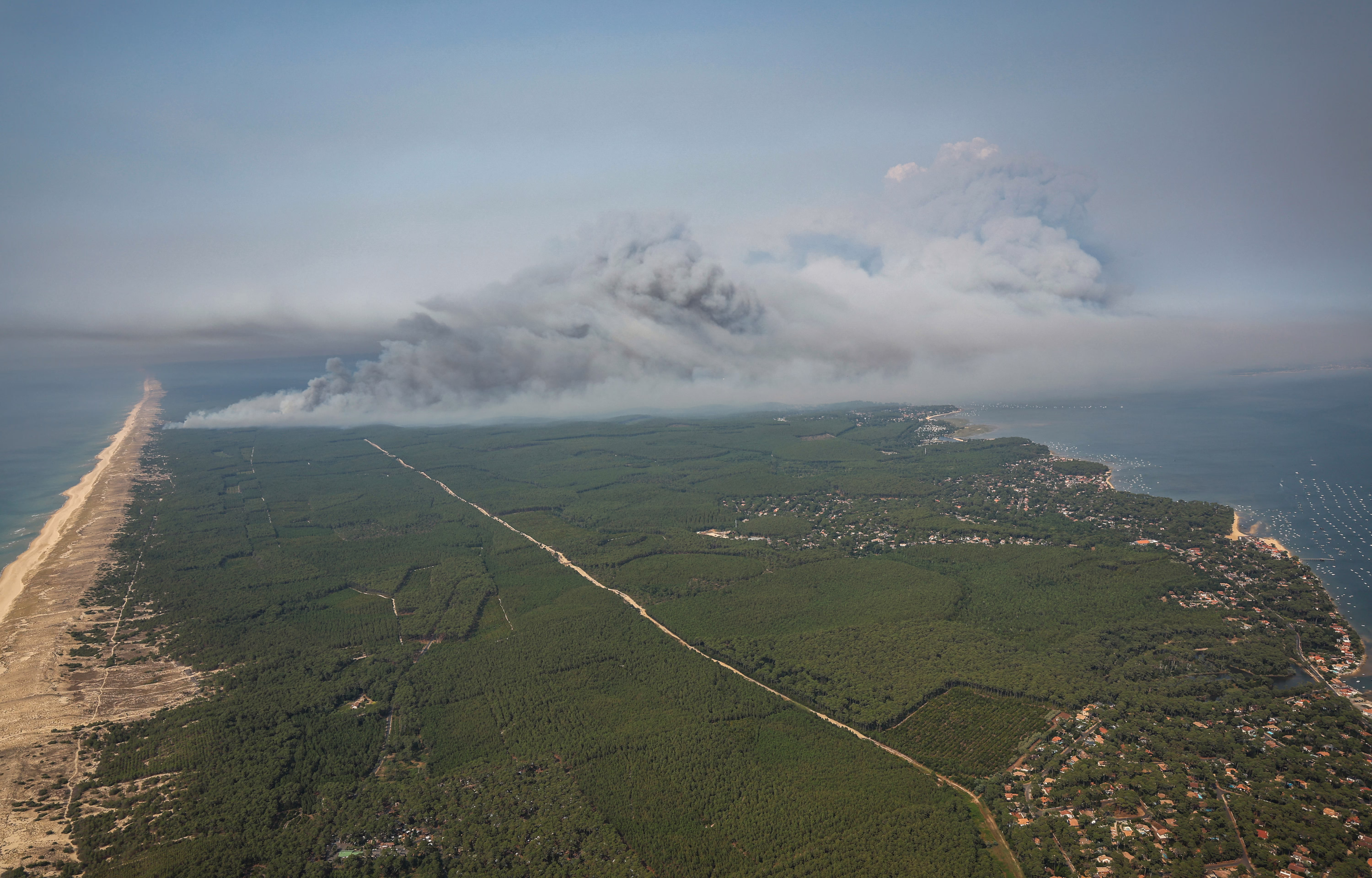 An aerial photograph showing smoke rising from a wildfire near a coastline.