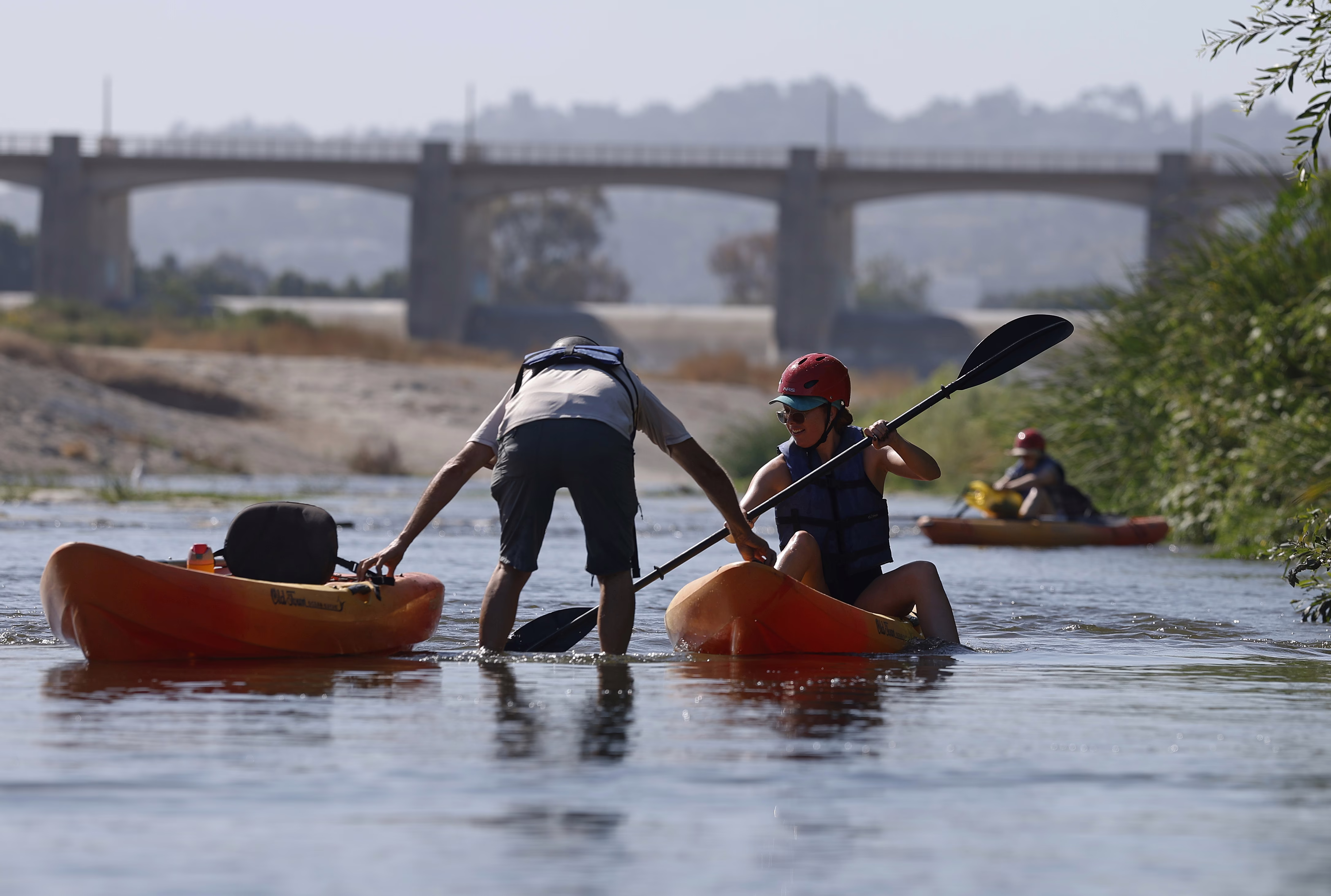 A person stands in shallow water, assisting a kayaker at the start of a tour.