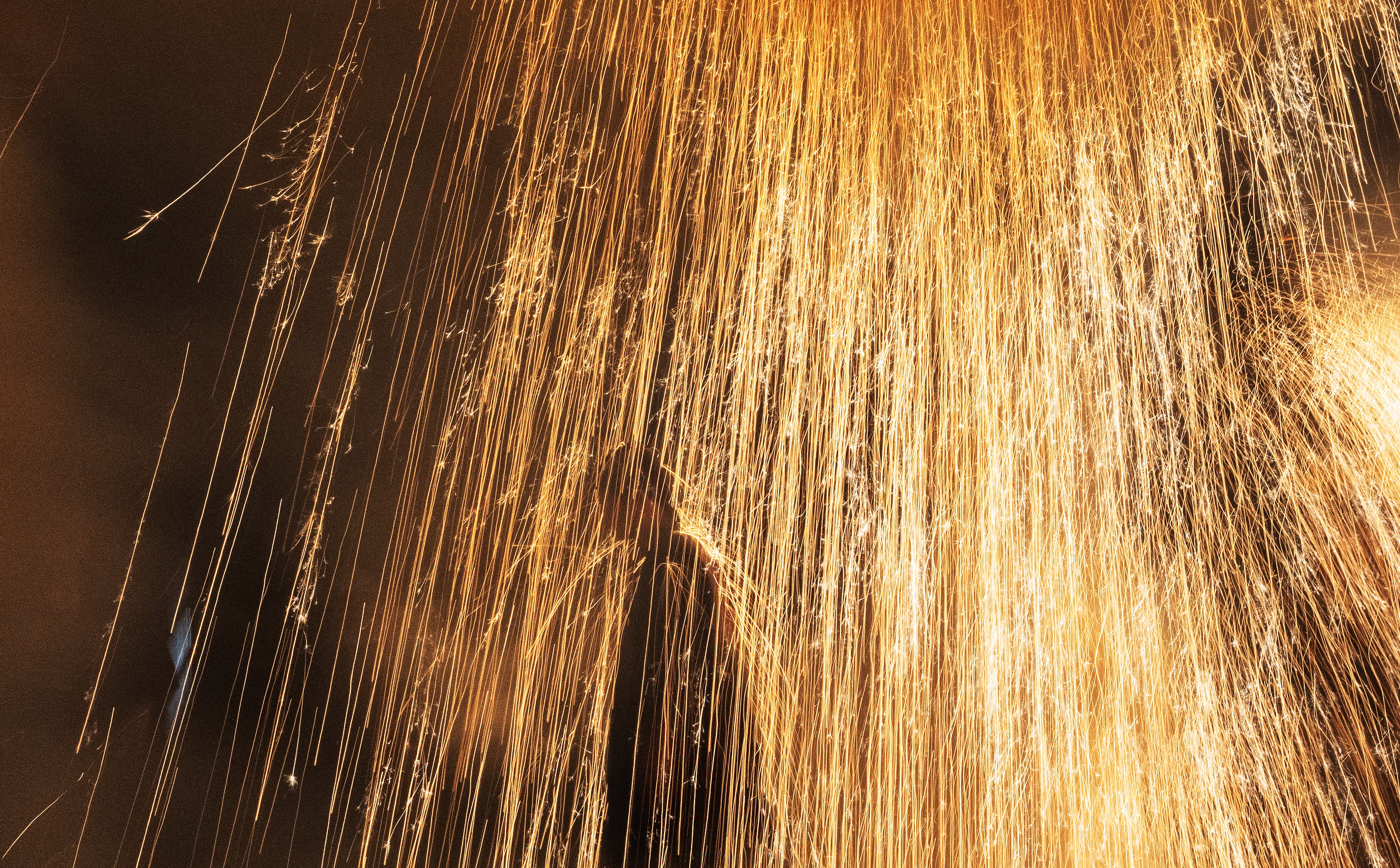 A performer stands under a huge shower of sparks, with some bouncing off their head and shoulders.