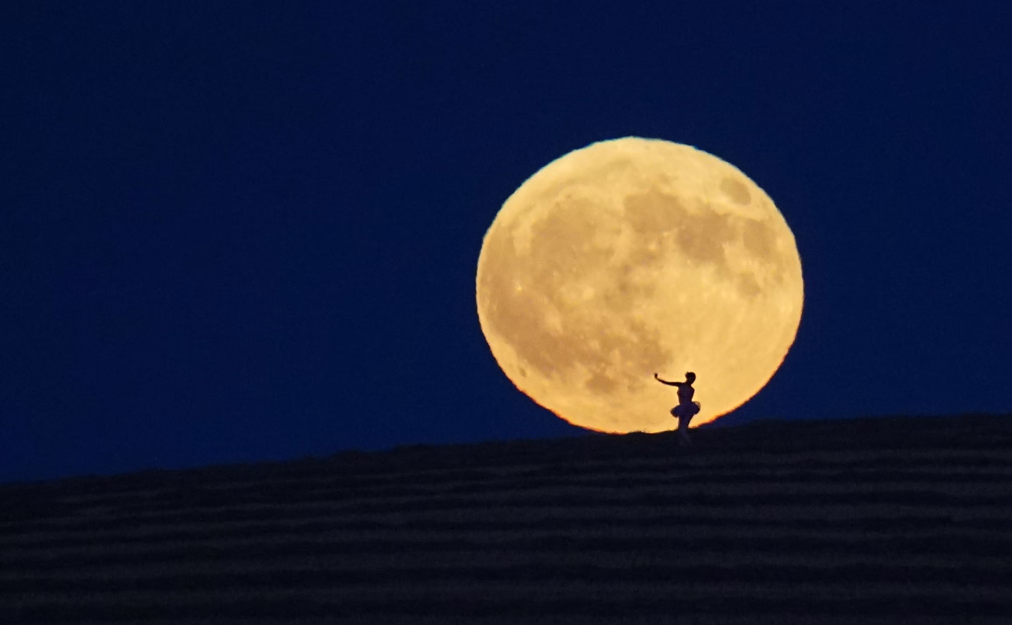 A ballerina performs, silhouetted against the full moon.