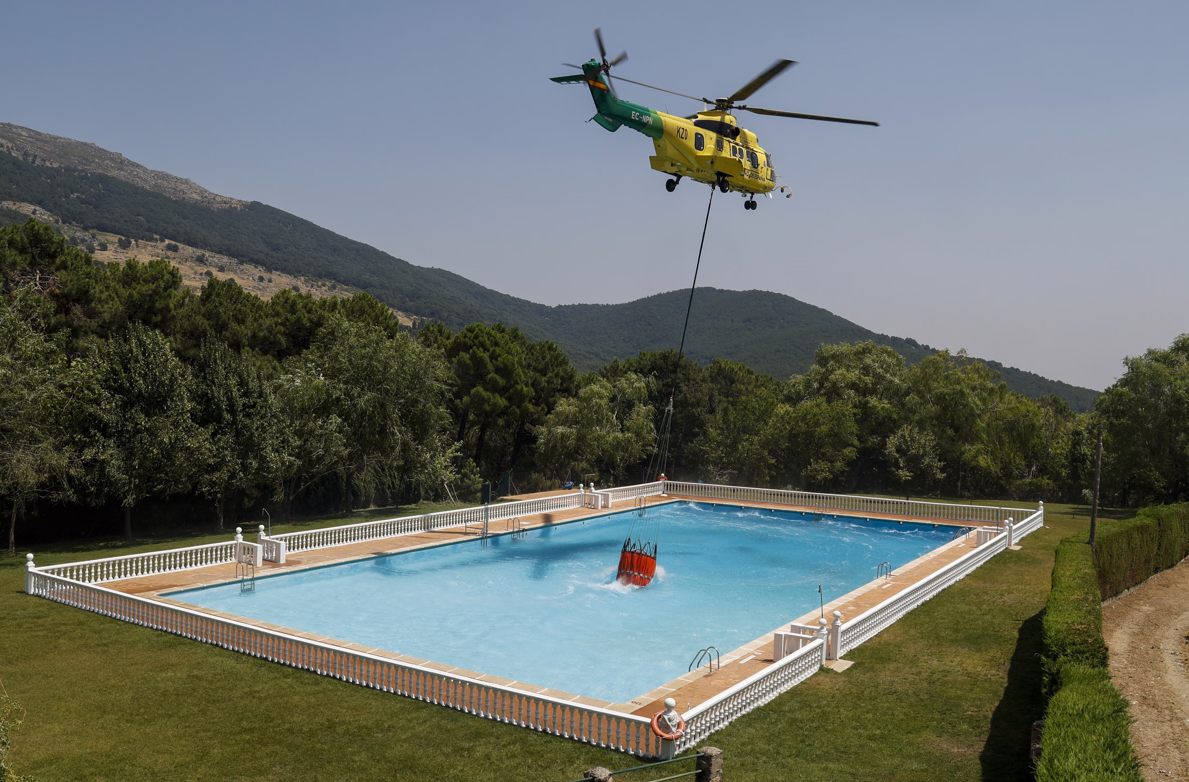 A helicopter uses a bucket hanging from a cable to collect water from a swimming pool to combat wildfires.