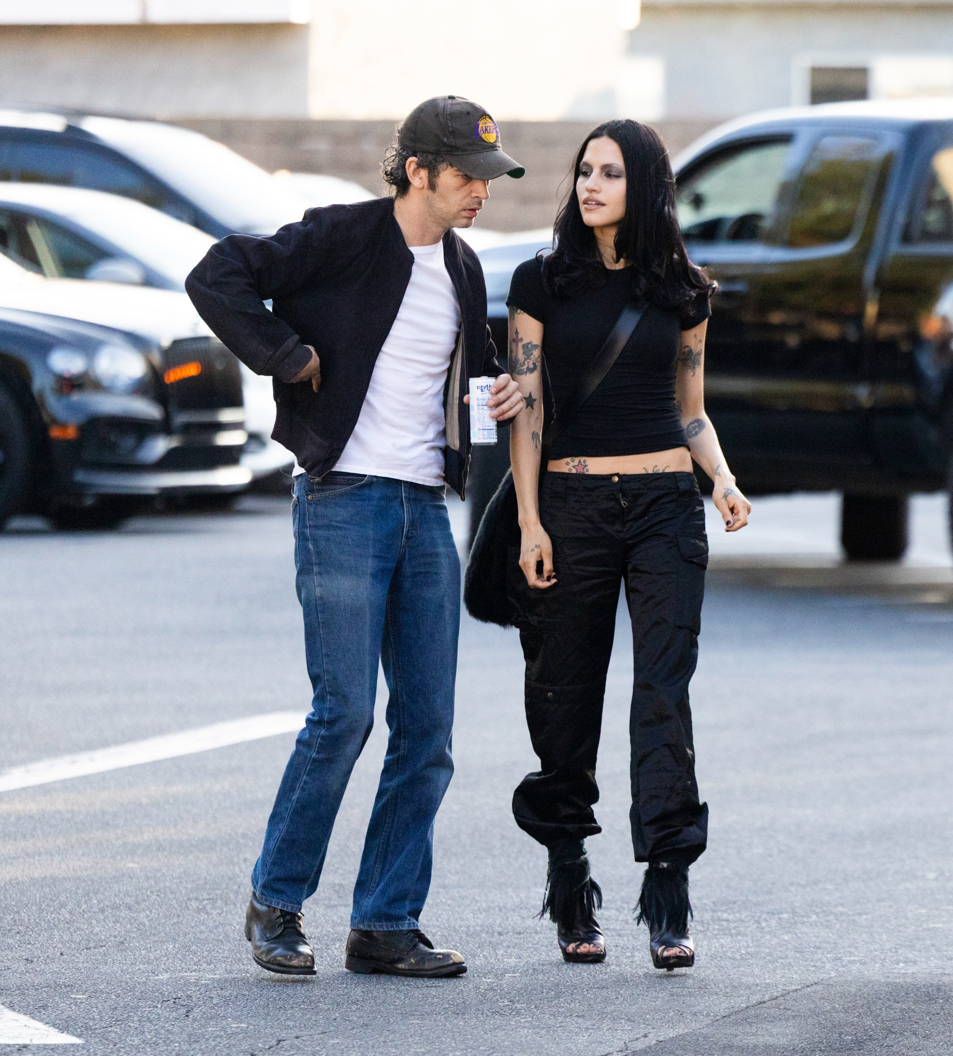 Matty Healy and Gabbriette Bechtel walking side by side, dressed in casual dark clothing and looking at each other.