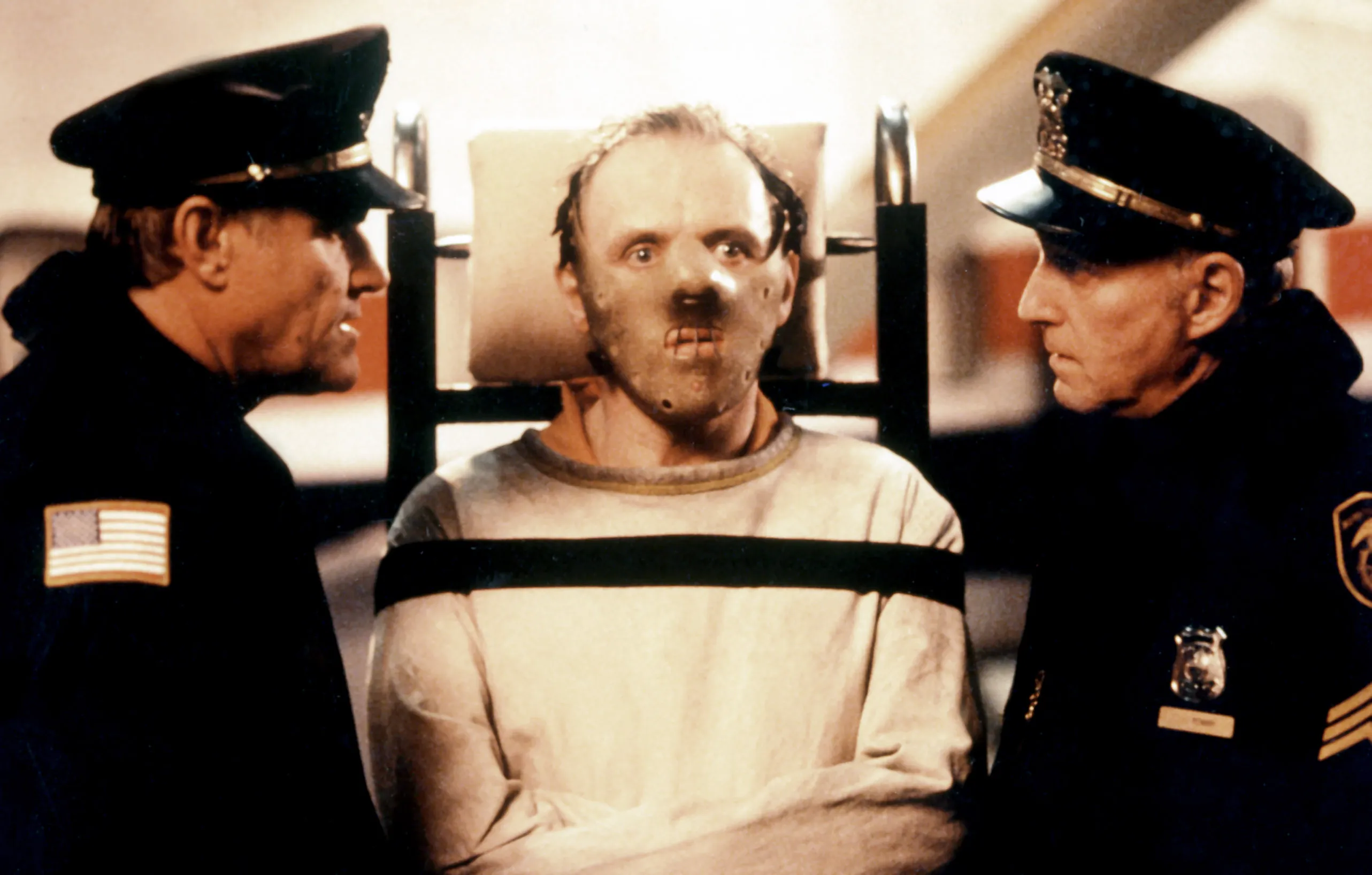 Anthony Hopkins as Hannibal Lecter in "The Silence of the Lambs," between two policemen, strapped into a straitjacket and wearing a muzzle.