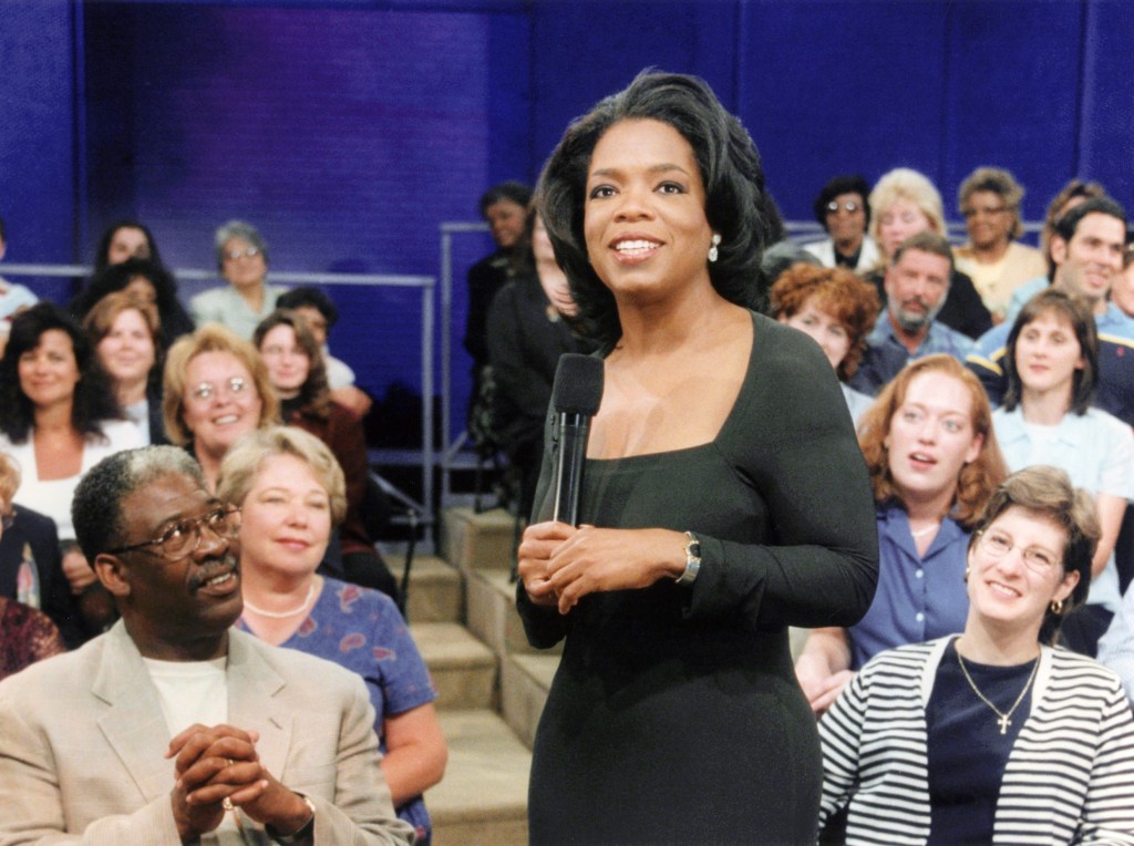 Oprah Winfrey holding a microphone, surrounded by her studio audience.