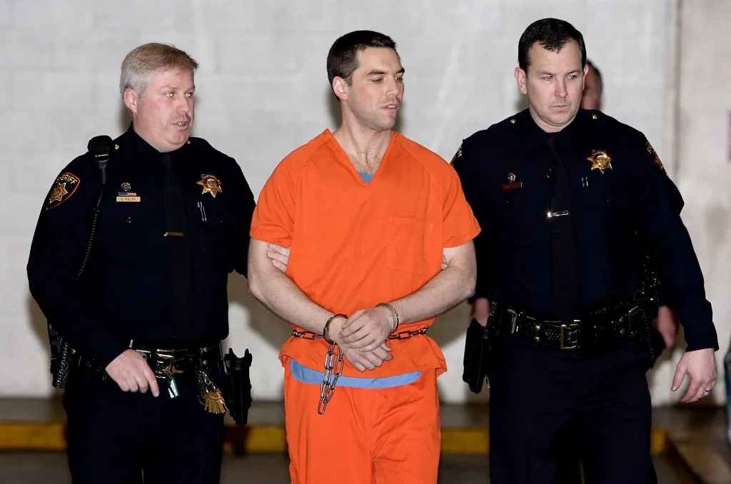 Convicted murderer Scott Peterson in an orange jumpsuit, handcuffed and escorted by two sheriff deputies.