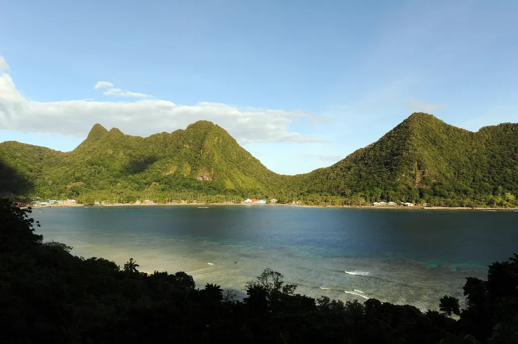 Vatia village in American Samoa, nestled along a coral-fringed bay, with lush, green mountains rising behind it.