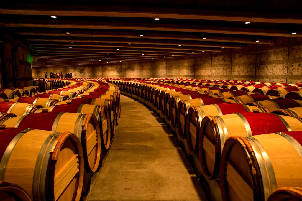 Oak barrels with red tops line a dim winery cellar.