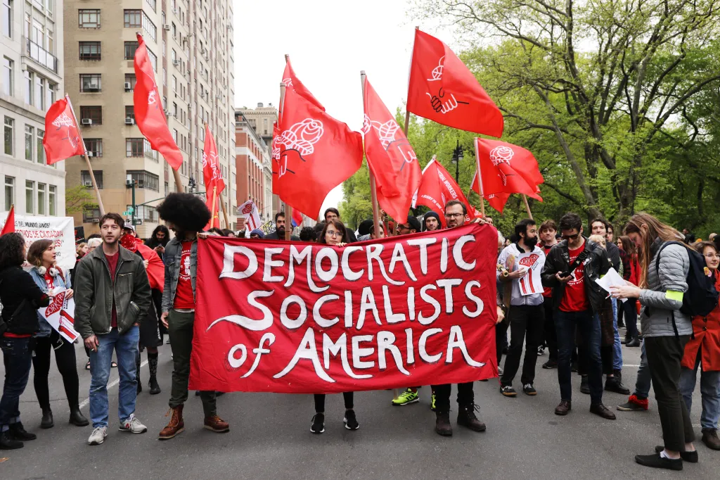 People marching with red flags and a large red banner that reads "Democratic Socialists of America."