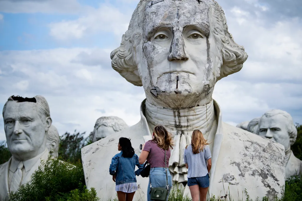 Three people view decaying busts of former US Presidents George Washington and Lyndon Johnson.