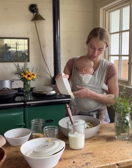 Hannah Neeleman, Mrs. Utah 2021, holding a baby in a carrier while cooking.