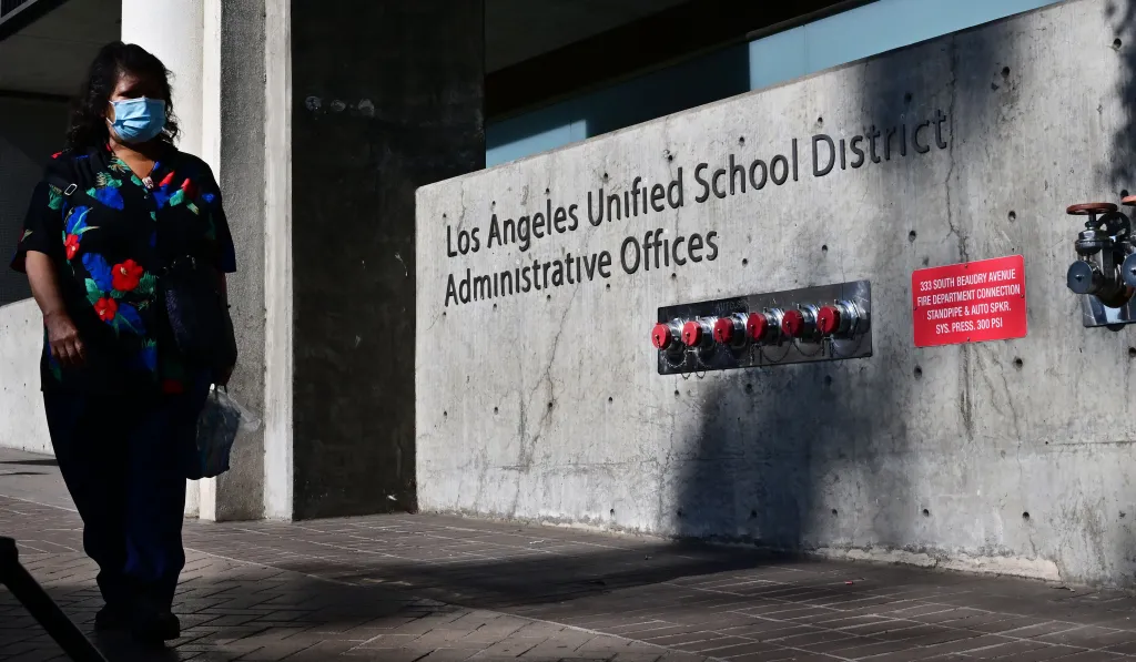 A pedestrian wearing a face mask walks past the Los Angeles Unified School District Administrative Offices.